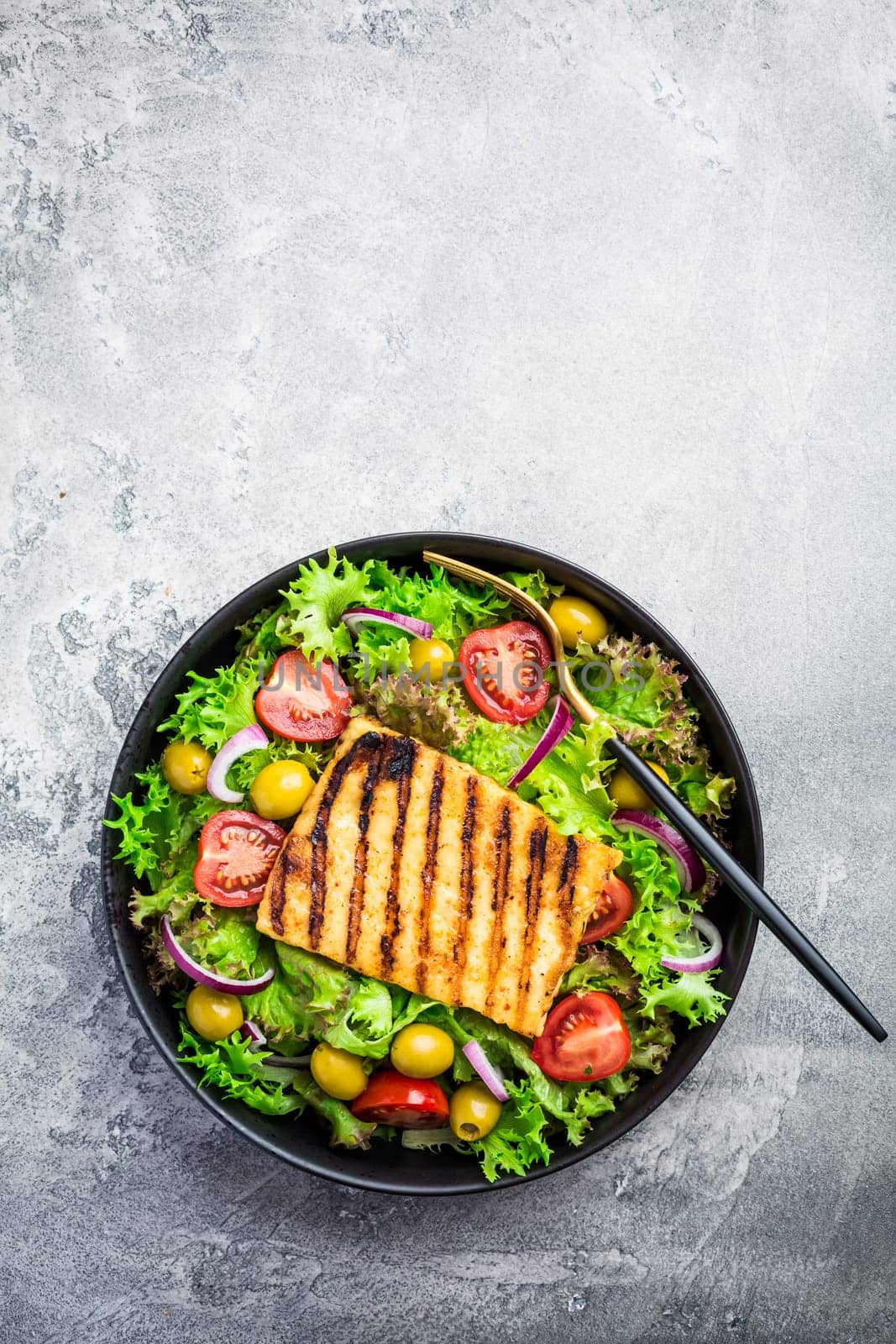 Fresh salad with grilled cheese, tomatoes and olives on grey