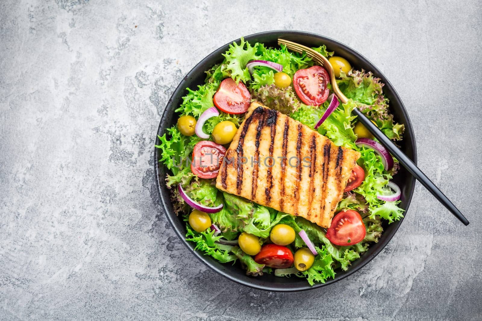 Fresh salad with grilled cheese, tomatoes and olives on grey
