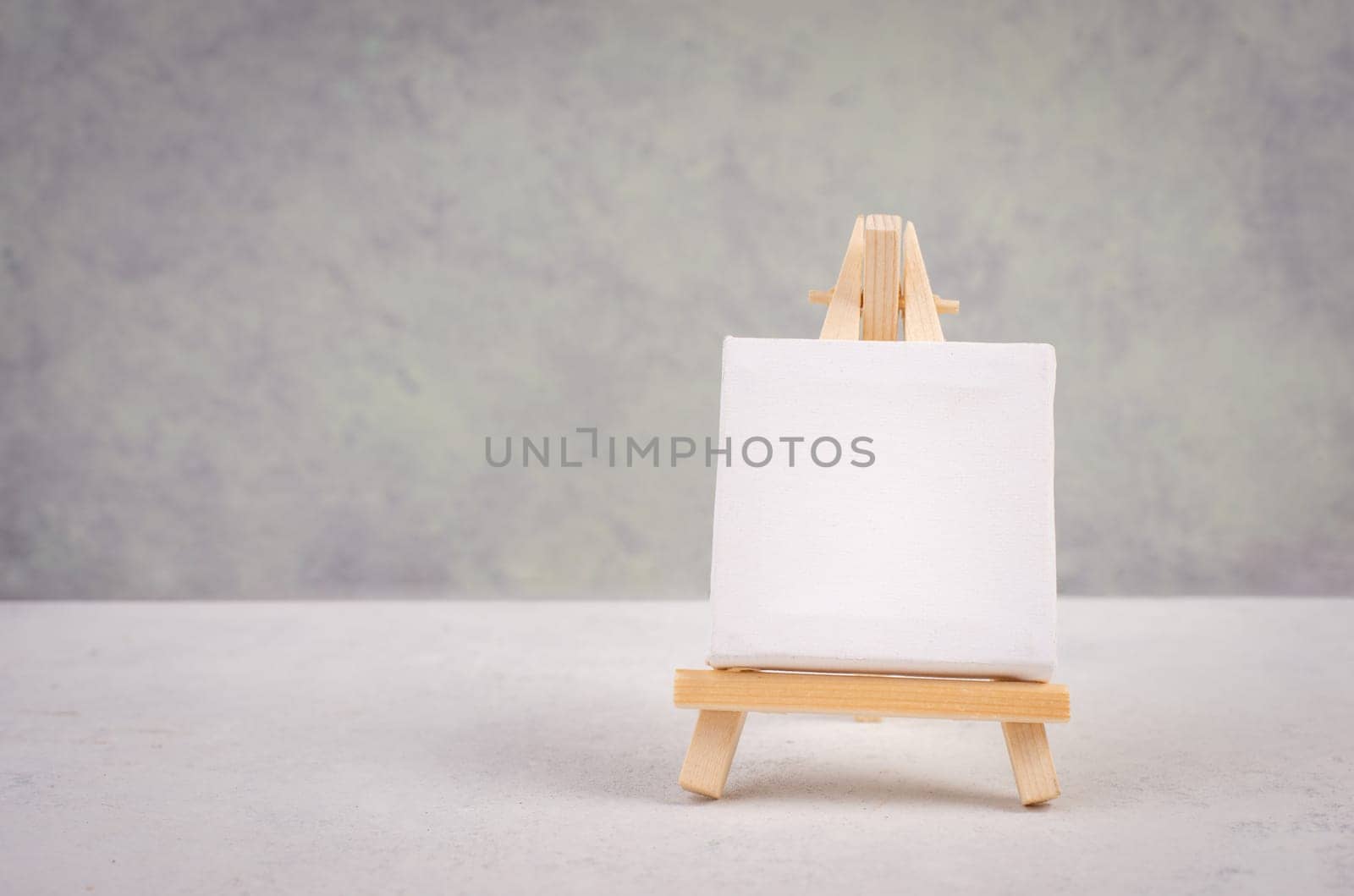 Easel with blank white canvas in front of a gray textured background, frame to add paintings and pictures
