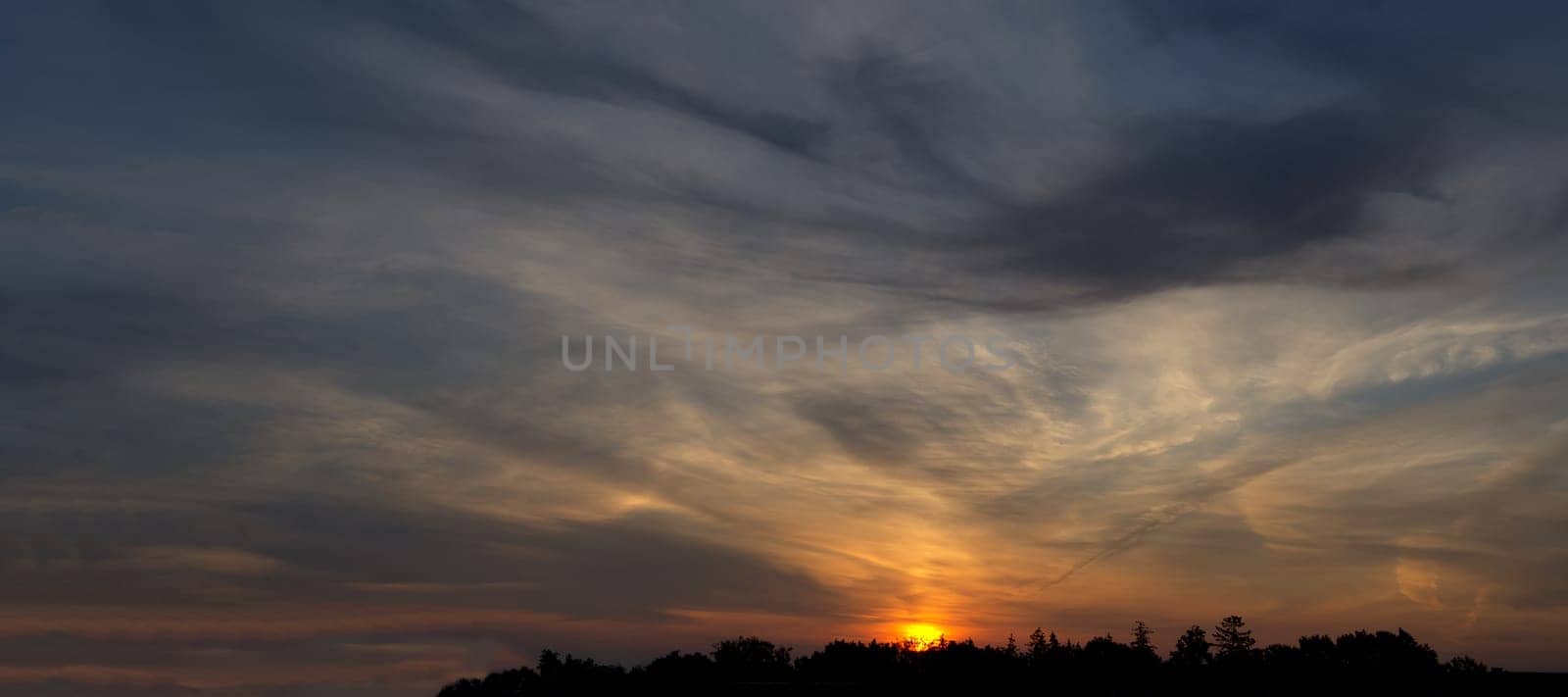 Scenic panorama view of colorful sunset with multicolor clouds, glowing sun peeking through the clouds