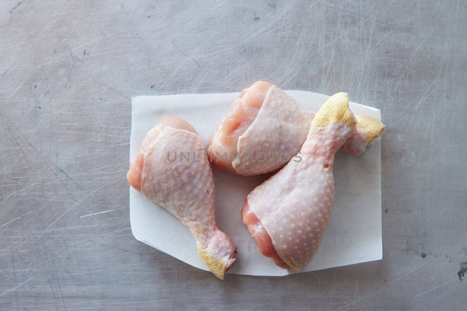 Top view of uncooked chicken drumsticks on napkin placed on gray background in light kitchen during cooking preparation at home