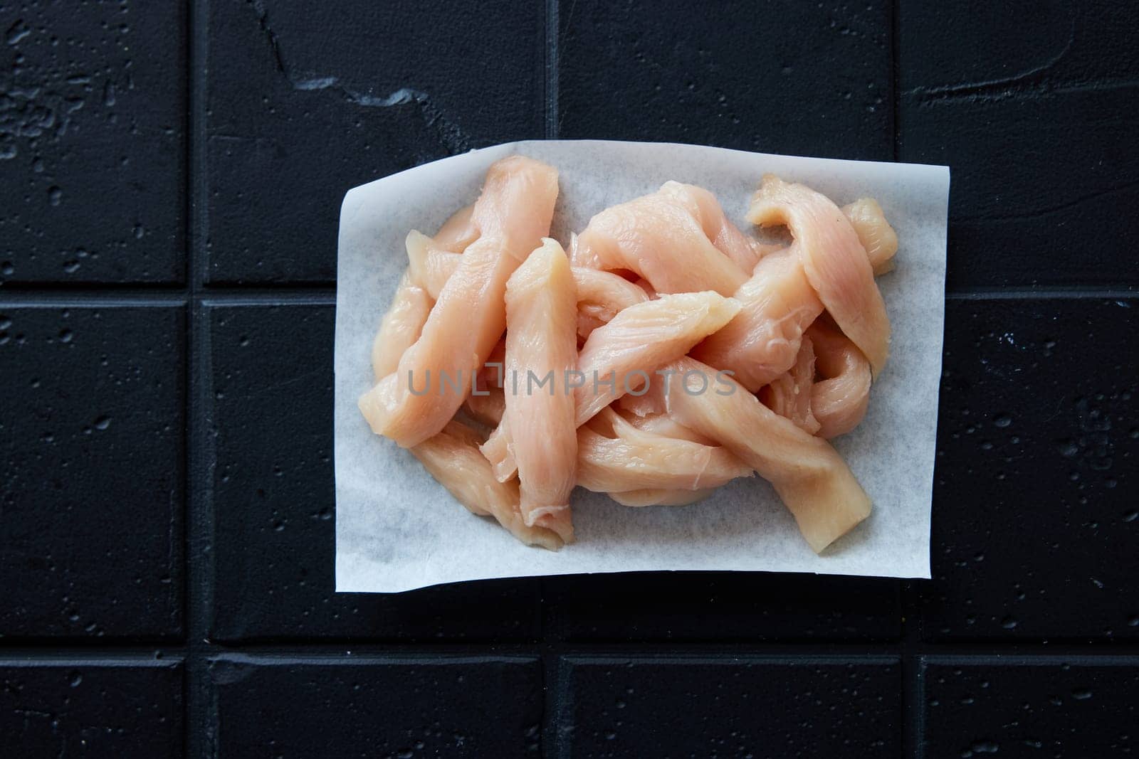 Top view of uncooked fresh chicken strips on white napkin placed on black background in light kitchen during cooking process