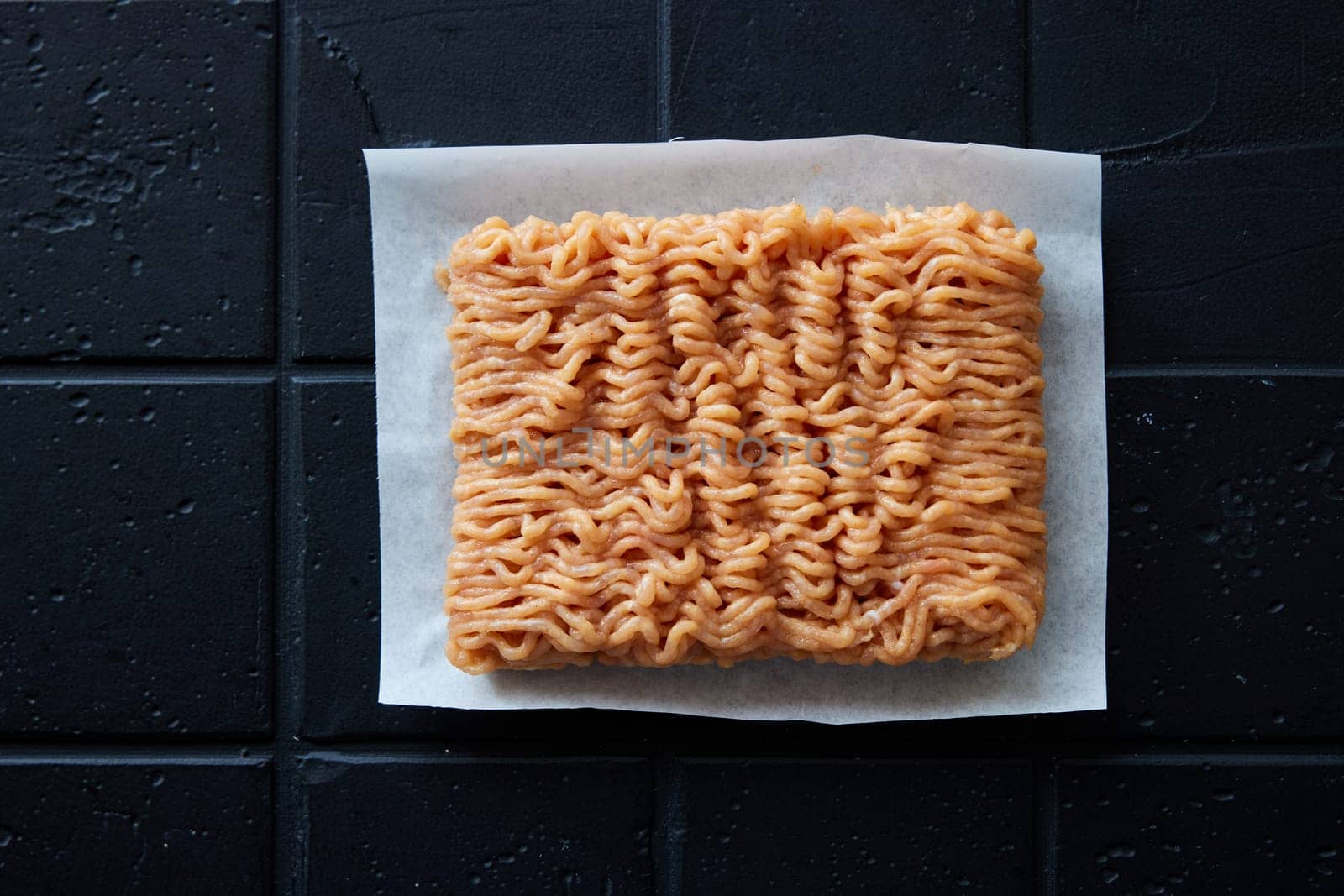 Top view of uncooked fresh chicken ground meat placed on napkin on black background in light kitchen during cooking preparation