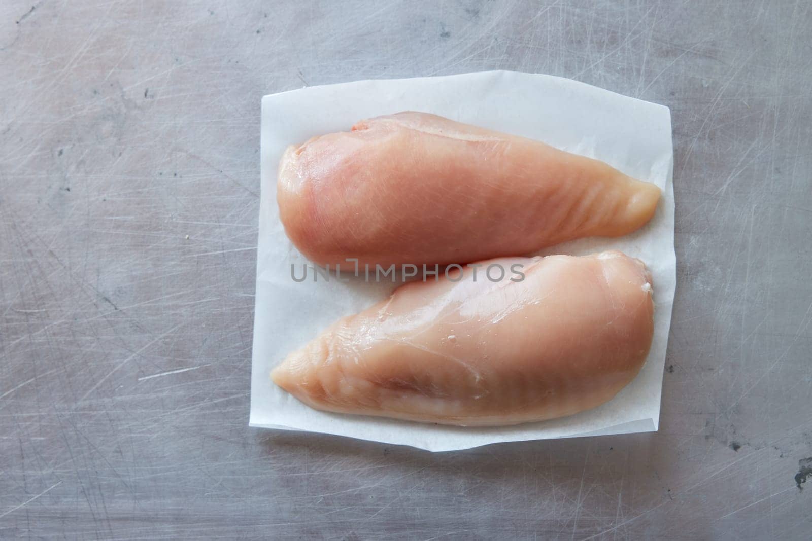Top view of uncooked fresh chicken breasts on white napkin placed on gray background in light kitchen during cooking process