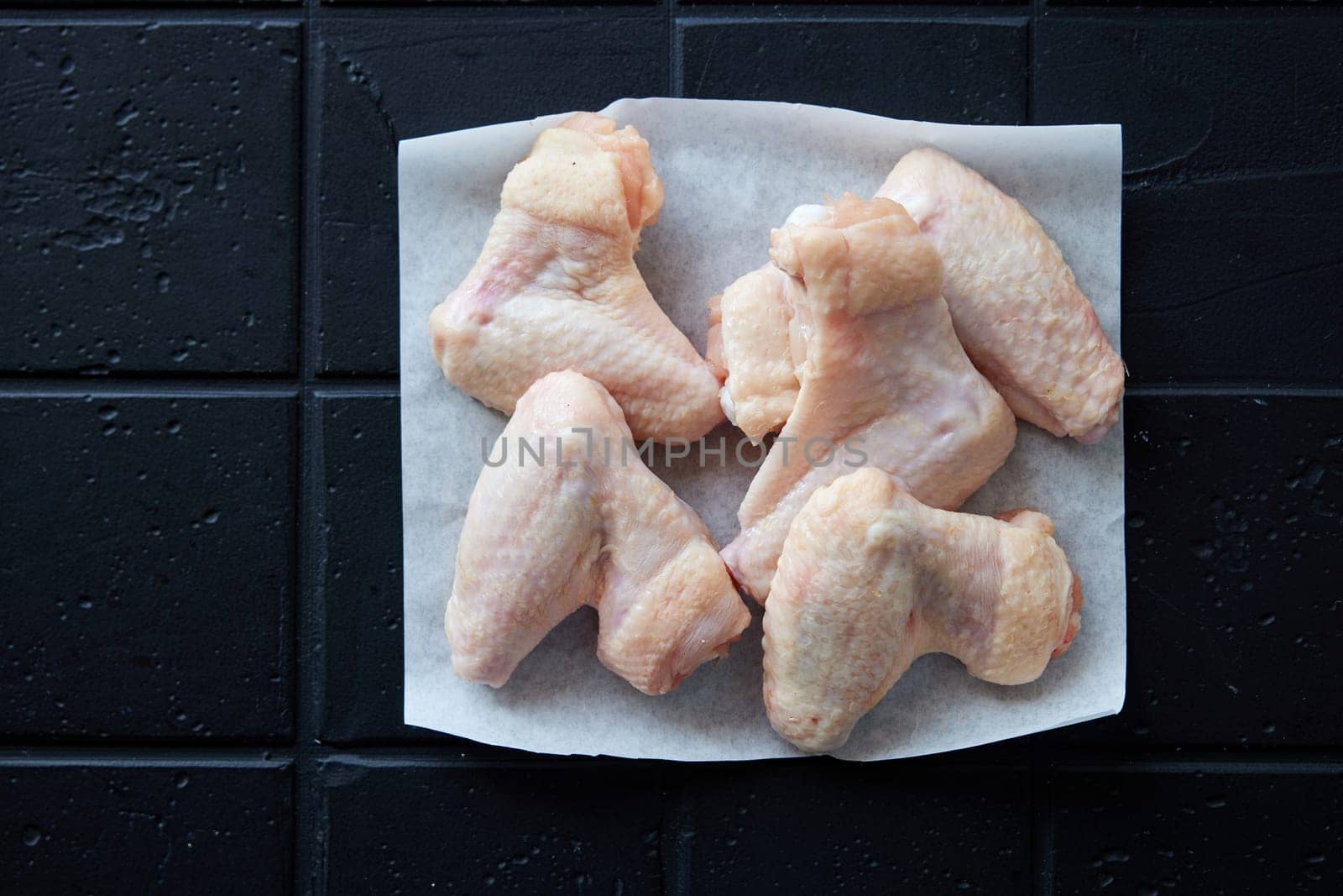 Top view of many raw chicken wings placed on tiled black background in light kitchen during cooking preparation at home