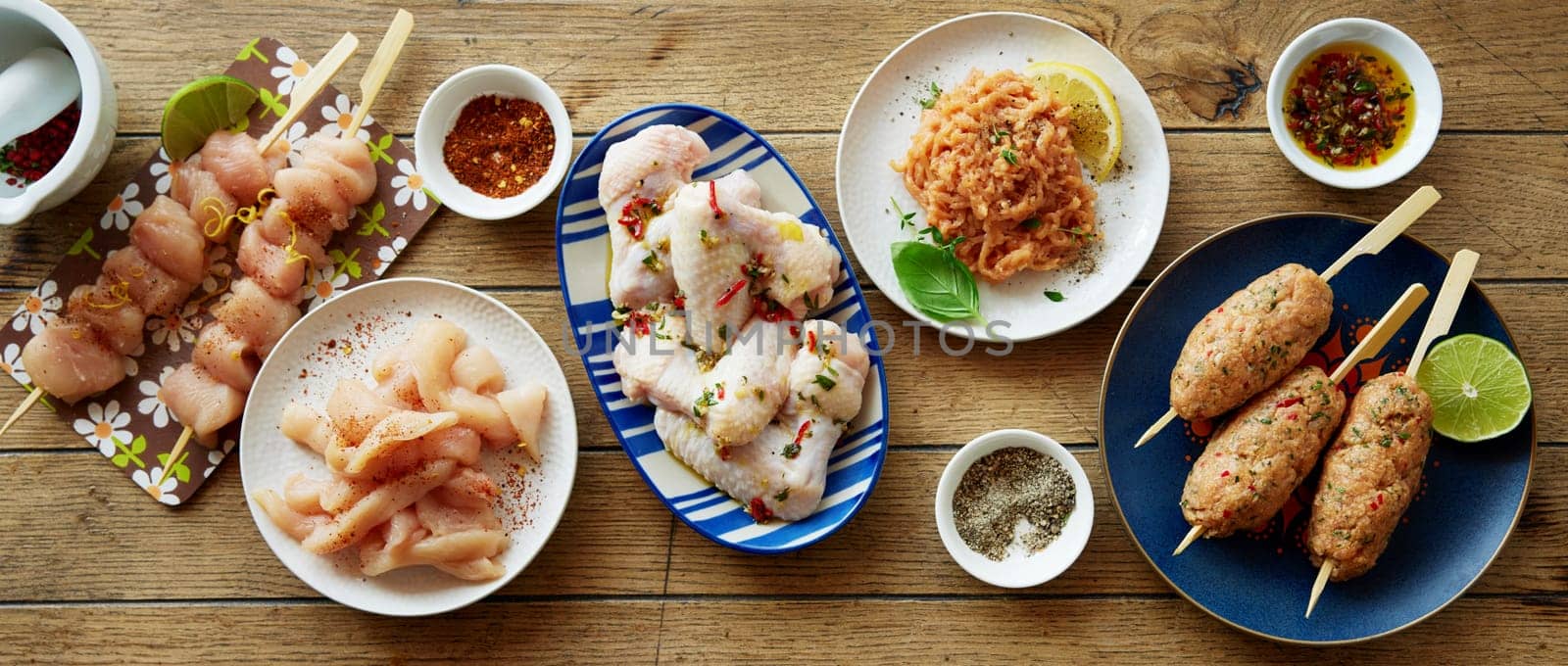 Top view mix of uncooked chicken meat served on plates on wooden table with assorted spices and condiments in kitchen