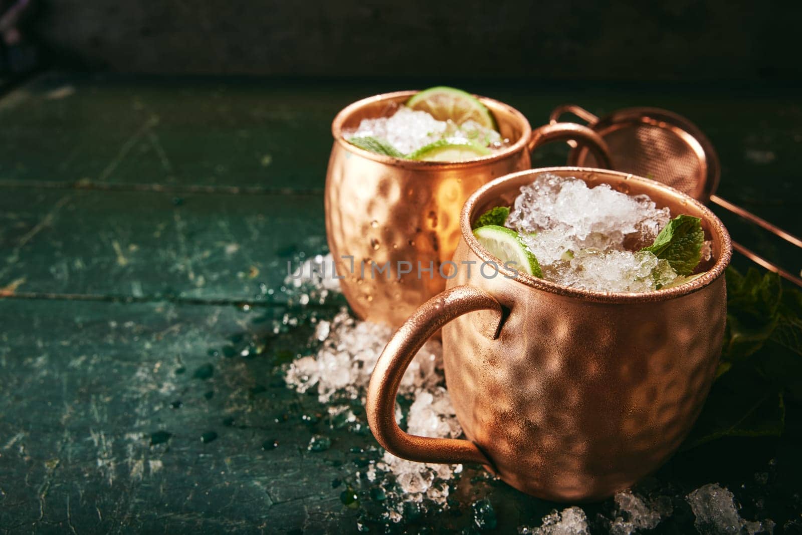 Refreshing alcoholic Moscow mule drinks with lime slices in copper cups placed on shabby table with ice in light kitchen