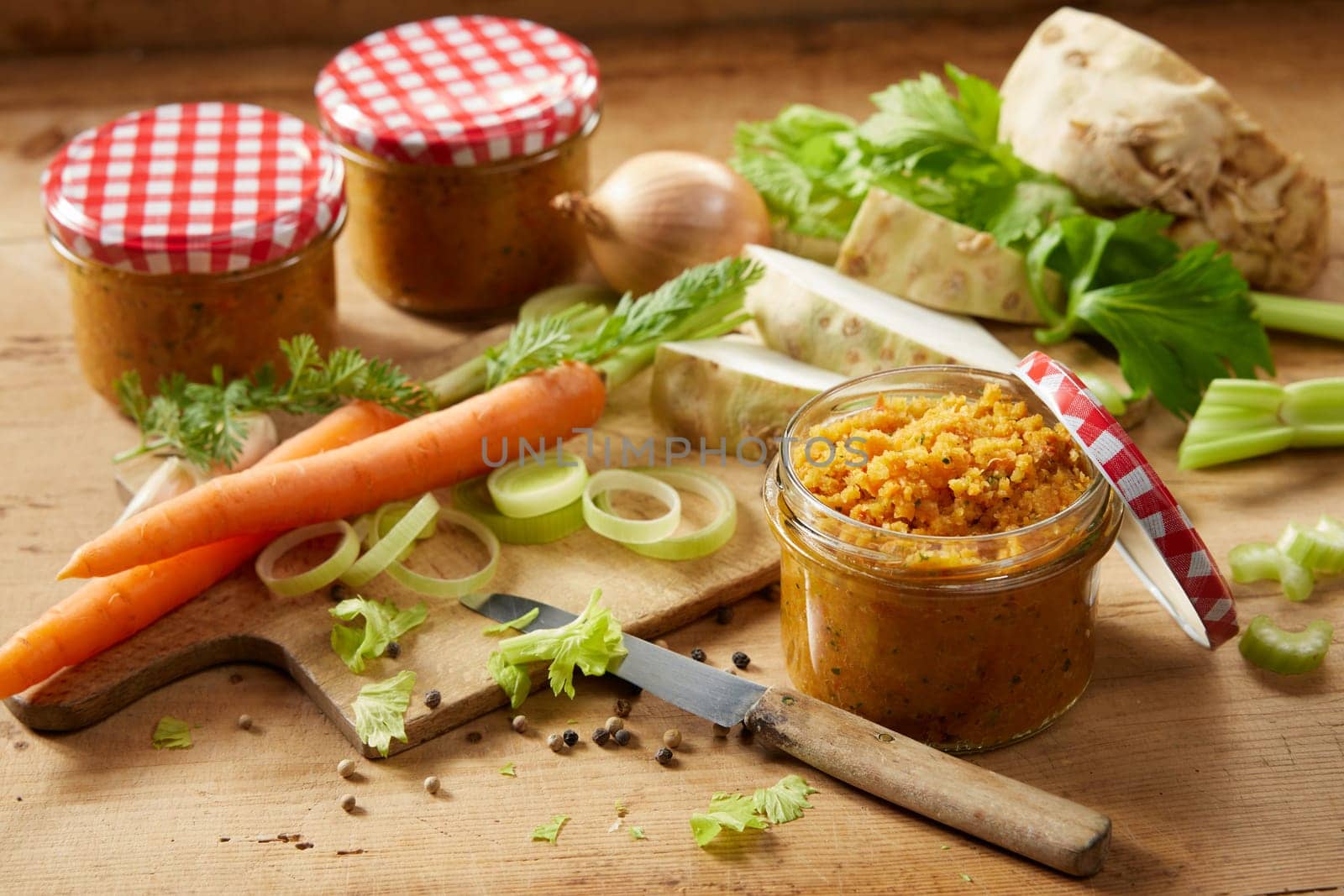 Glass jars filled with fresh vegetable conservation placed on wooden table with carrots and celery in light kitchen during cooking process