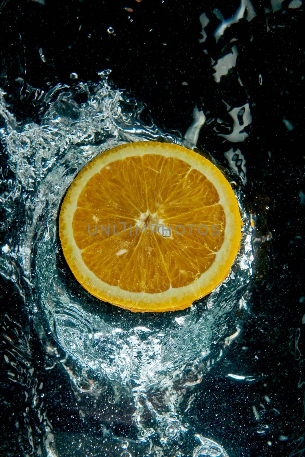 From above round slice of tasty ripe orange on water surface with splashes and water drops in modern light studio