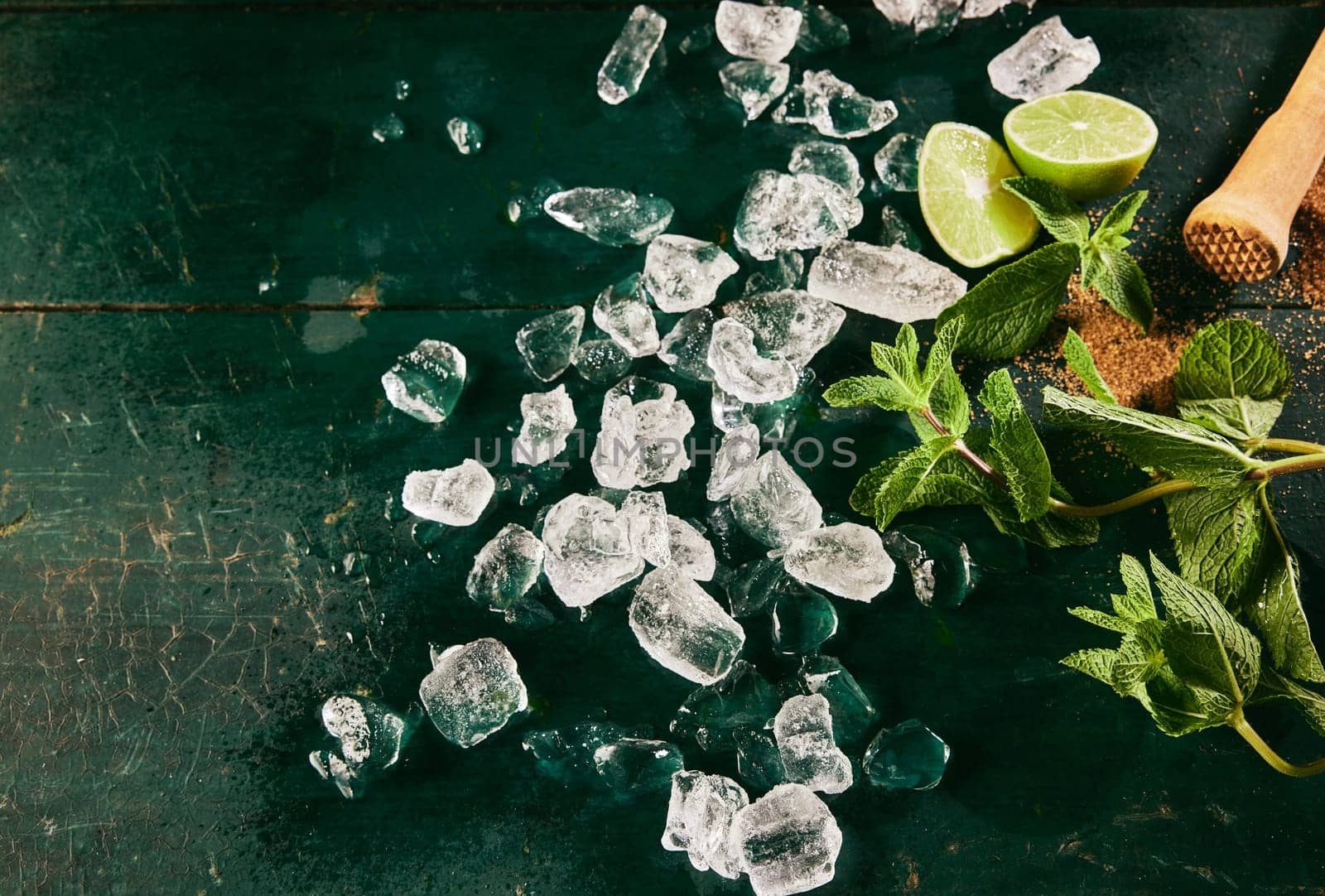 Top view of ingredients for mojito cocktail including heap of ice cubes scattered on shabby table with green mint leaves and fresh lime slices