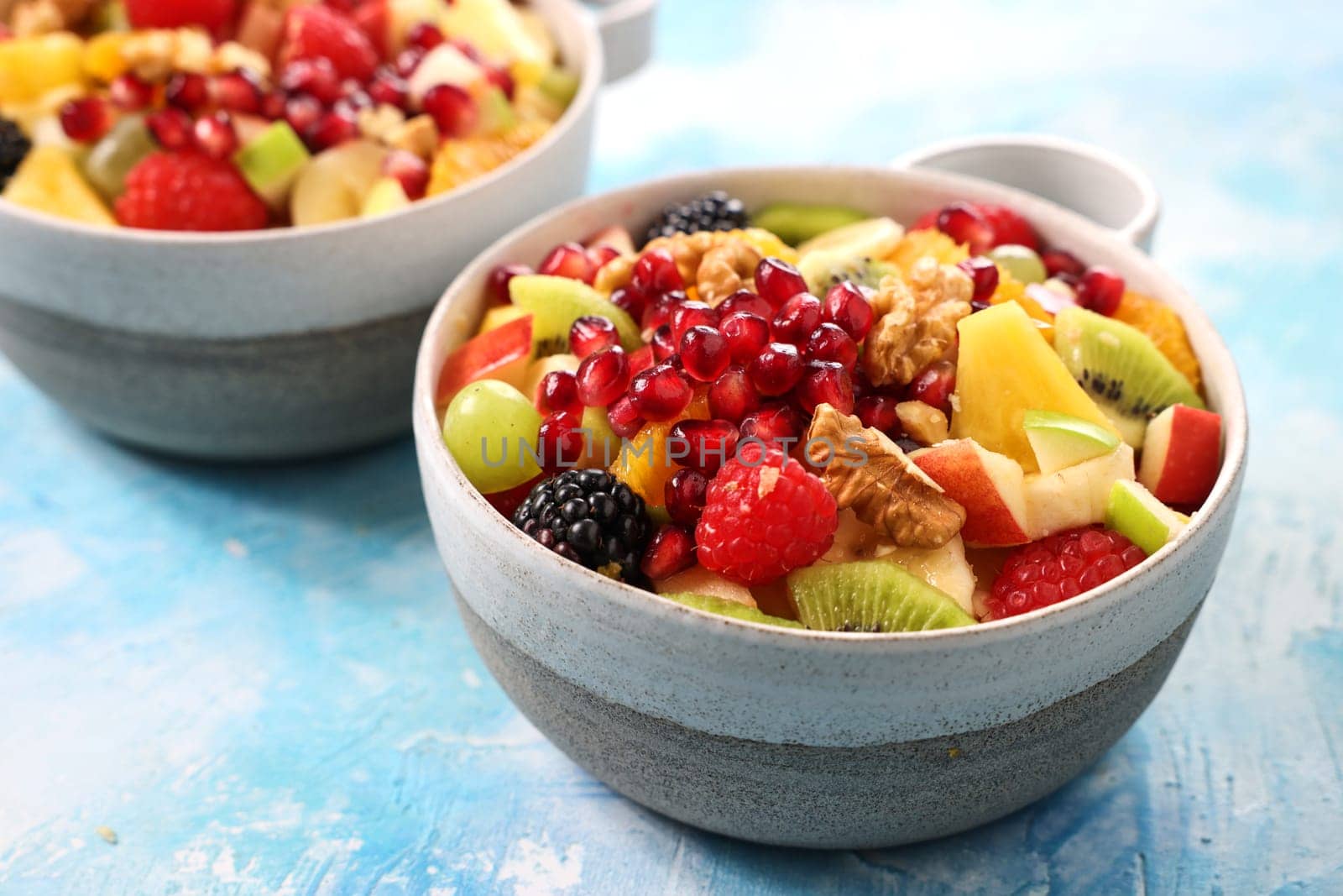 Mix of chopped ripe tasty fruits and berries topped with pomegranates and walnuts served in bowl on table in light kitchen