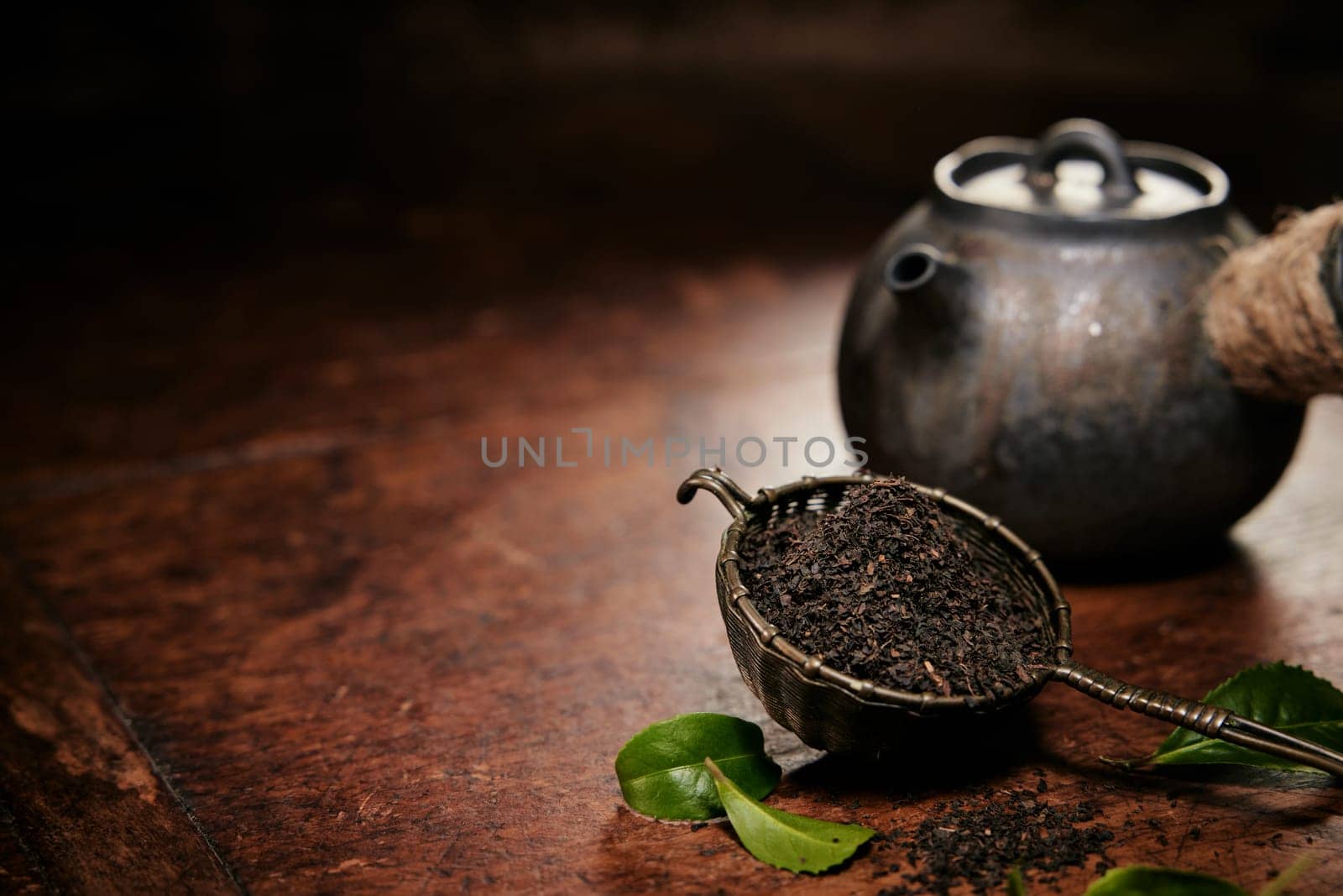 Aromatic loose tea fro brewing in metal ladle placed on table with leaves and old fashioned metal teapot in kitchen