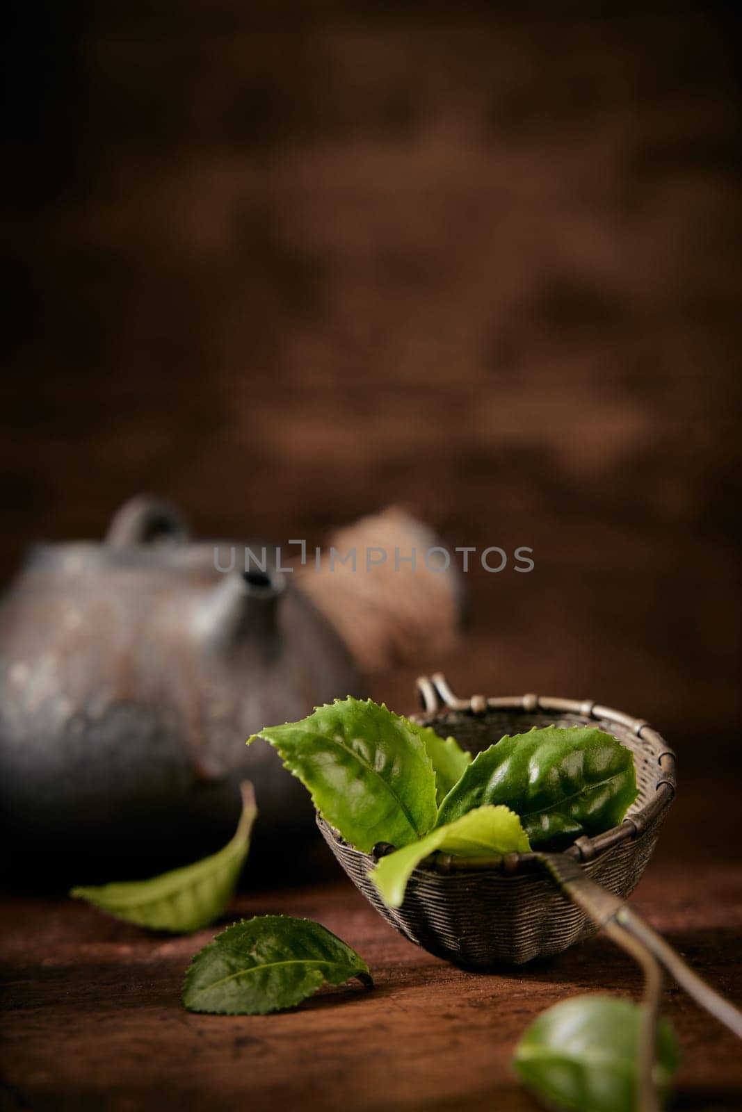 Green tea leaves for brewing in metal ladle placed on table with old teapot on blurred background in light room