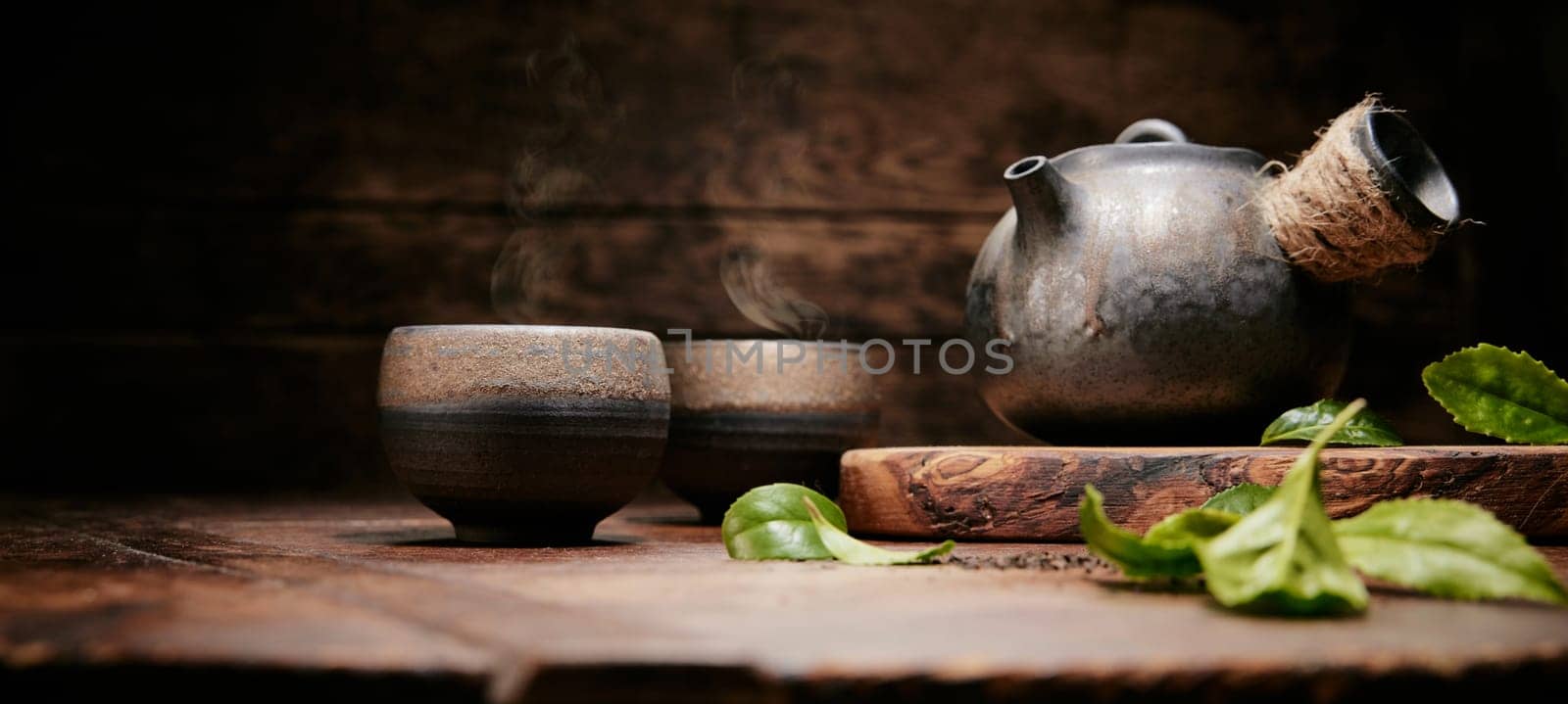 Green fresh tea leaves for brewing on wooden table with tea cup and retro metal teapot in kitchen during tea time