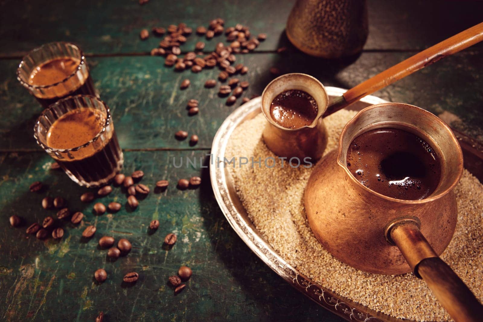 From above cezves on sand and glasses with hot traditional oriental coffee placed on table with scattered coffee beans in kitchen