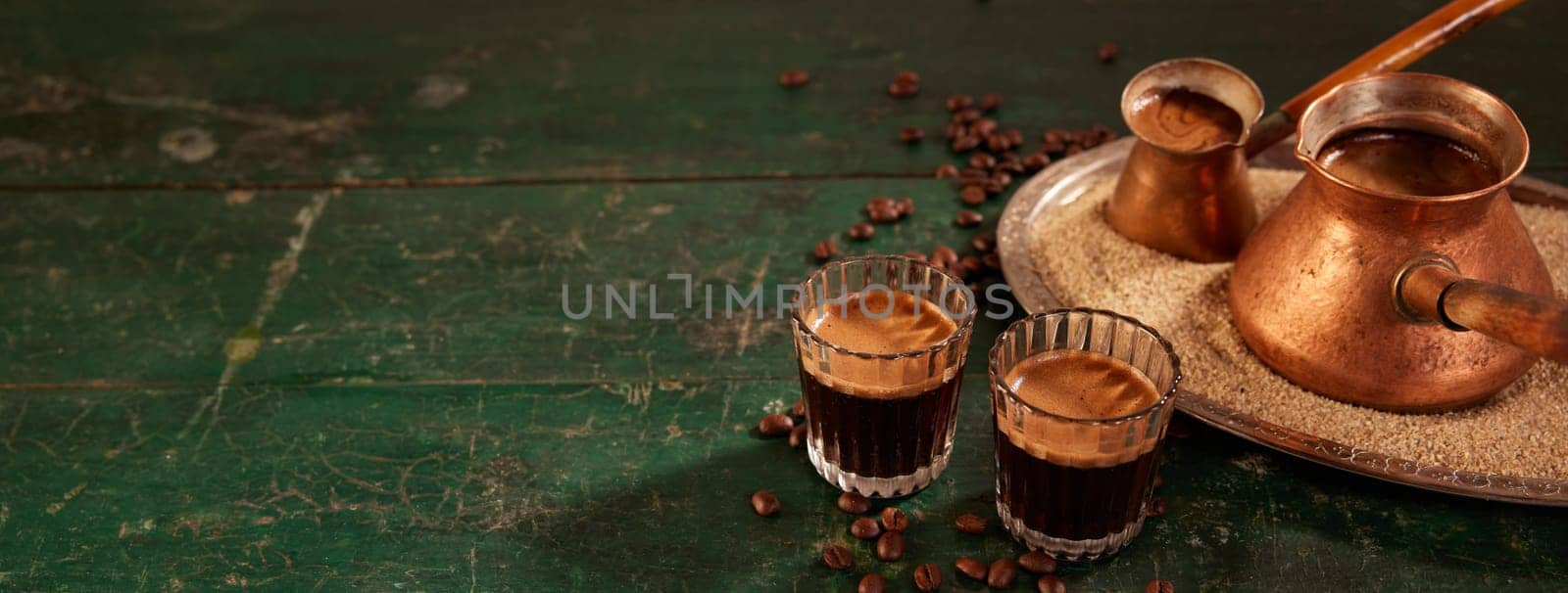 Glasses and cezves on sand with tasty freshly brewed coffee with froth placed on shabby green wooden table in kitchen