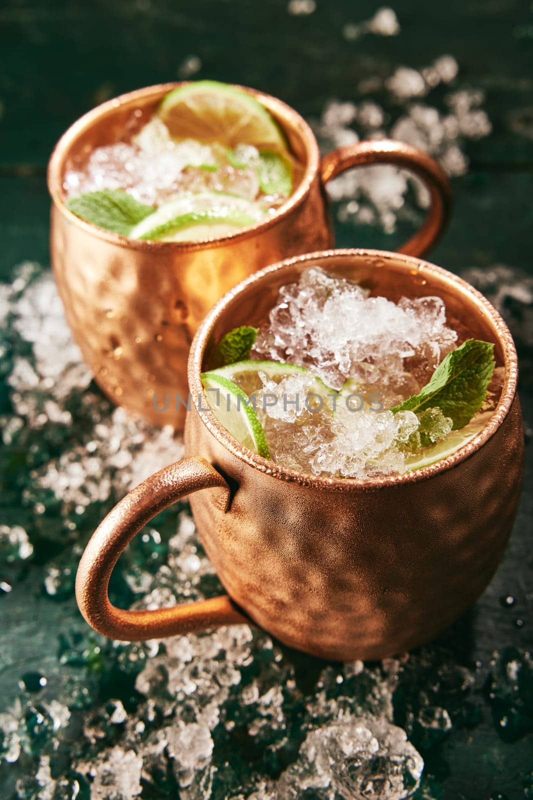 From above of alcoholic Moscow mule beverages with lime slices served in copper mugs on table with ice in kitchen