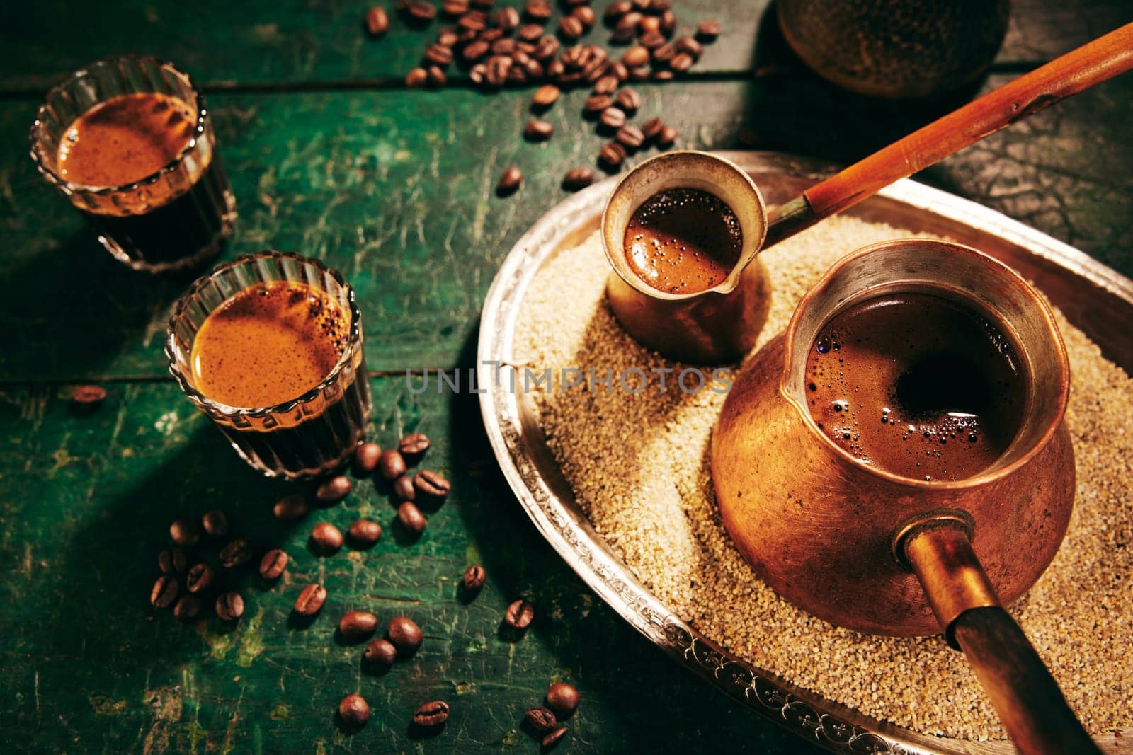 High angle of freshly brewed hot oriental coffee in cezves and glasses placed on shabby green table in light kitchen