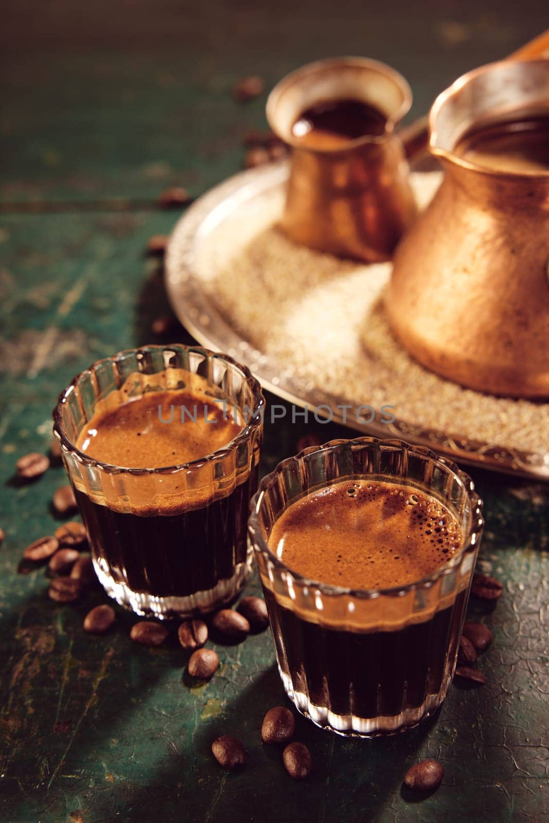 From above of Turkish hot coffee in glasses and cezves placed on shabby wooden table with scattered coffee beans in kitchen during break