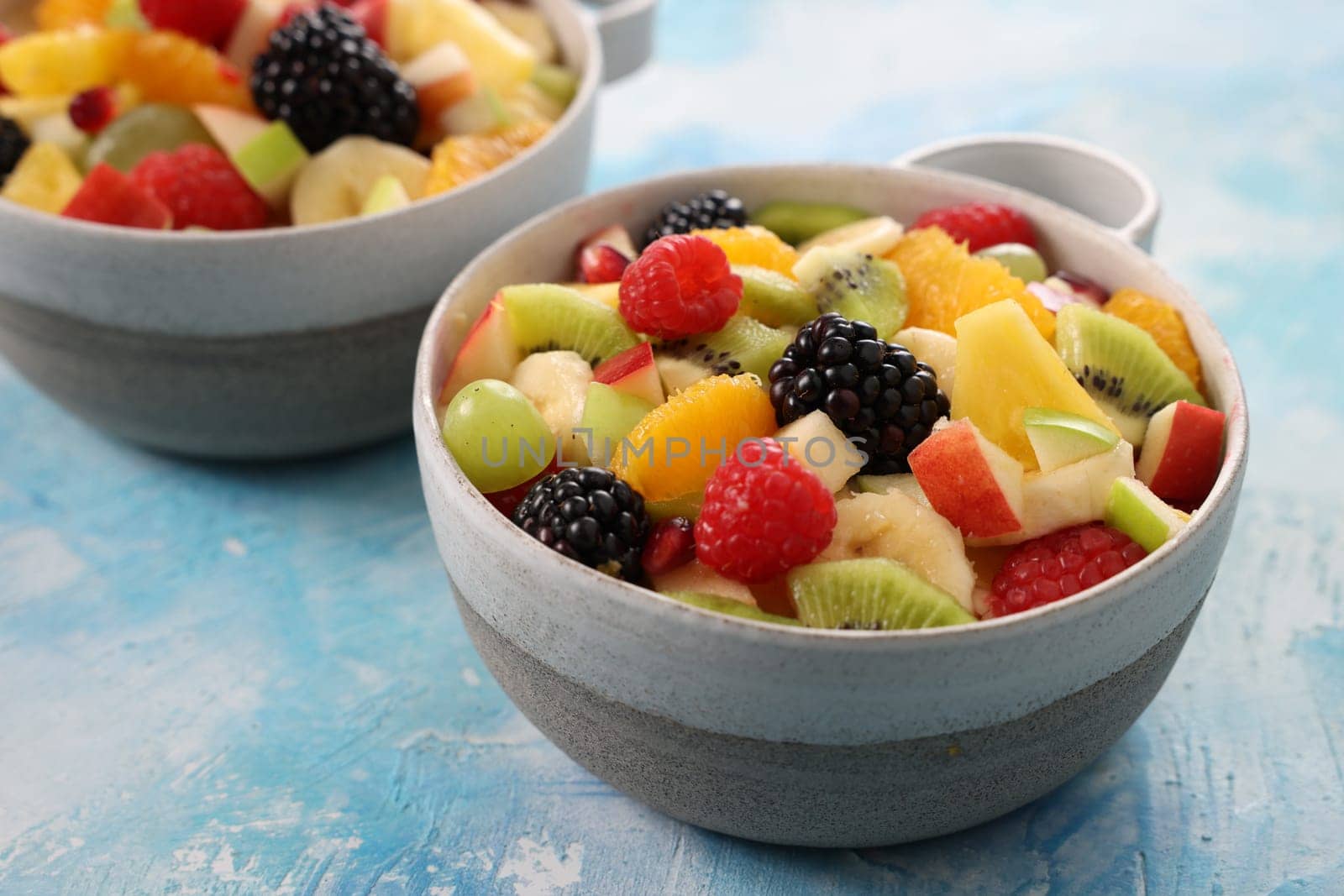 Fresh tasty chopped fruits and ripe colorful berries served in ceramic bowls on wooden table in light kitchen at home