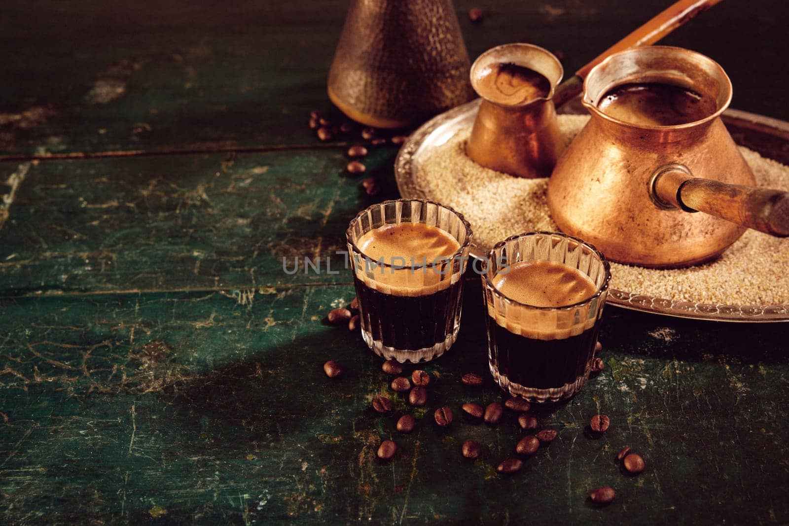 High angle of traditional hot oriental coffee in glasses and metal cezves served on weathered green wooden table in kitchen