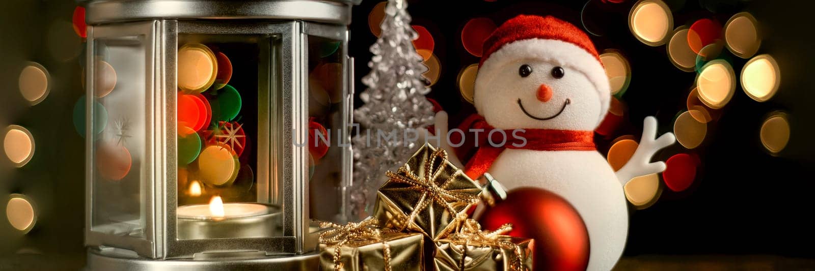 Christmas composition: A snowman, a lantern with candles, bright shiny boxes with gifts, blurred bokeh lights in the background.