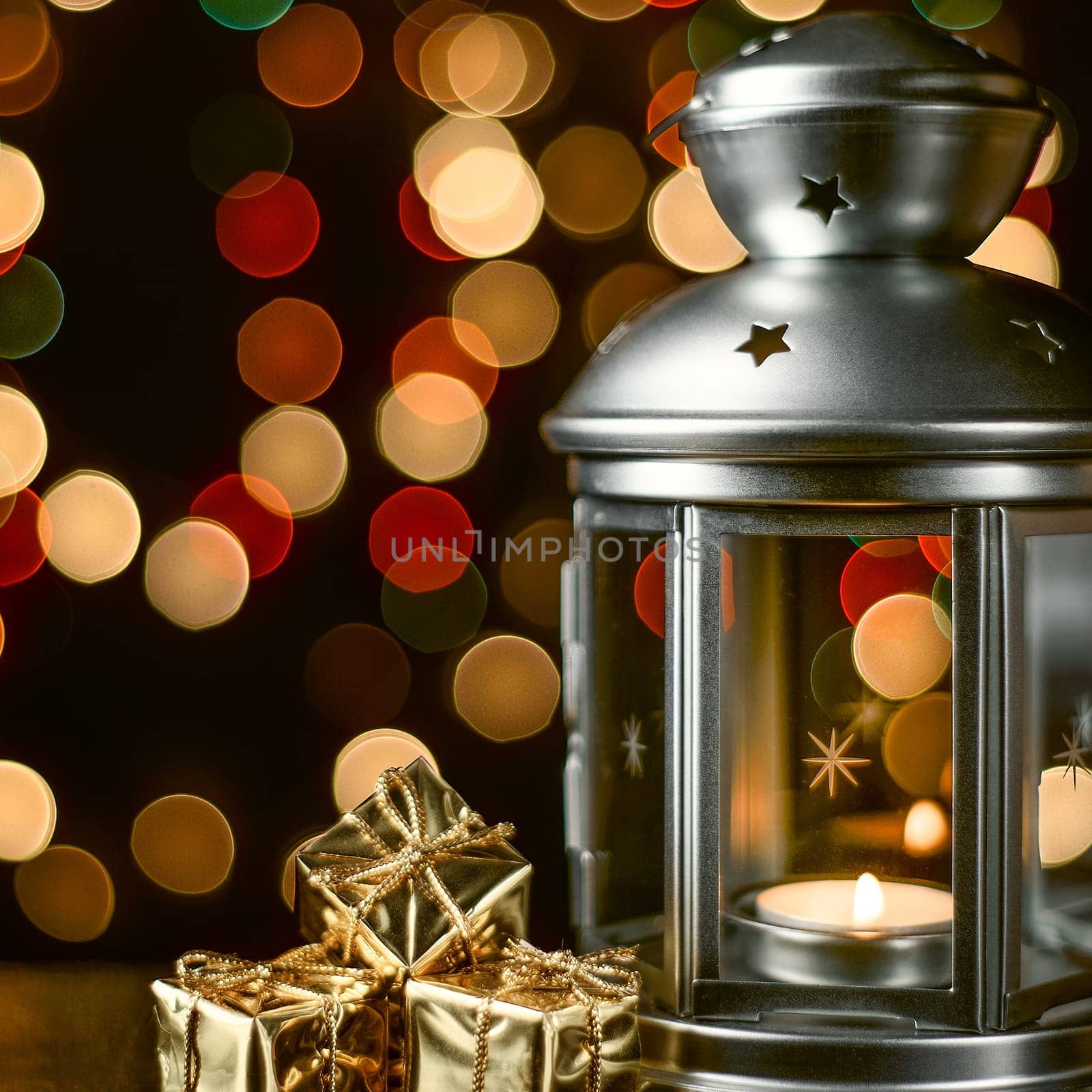 Christmas composition: a lantern with candles, bright shiny boxes with gifts, blurred bokeh lights in the background.
