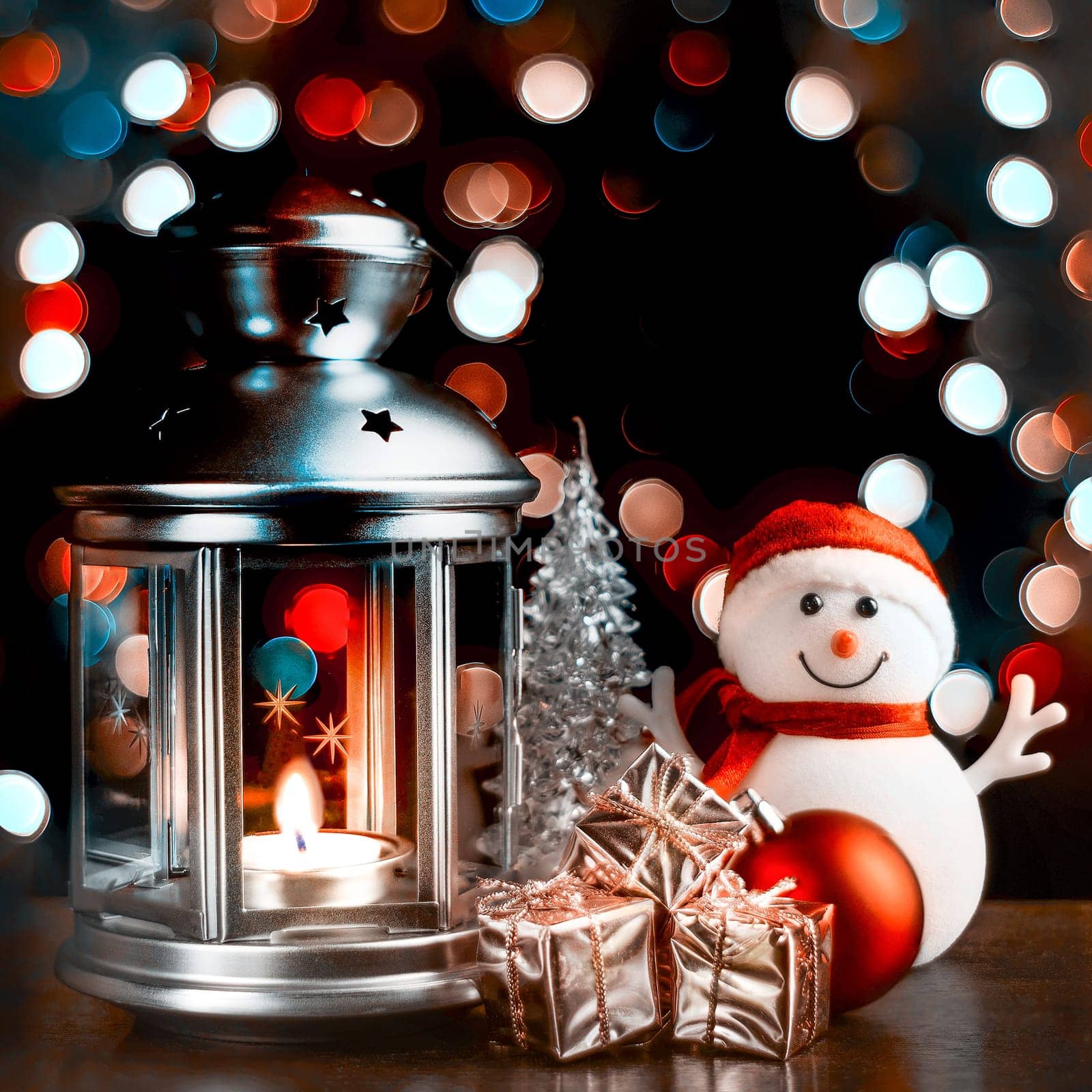 Christmas composition: A snowman, a lantern with candles, bright shiny boxes with gifts, blurred bokeh lights in the background.