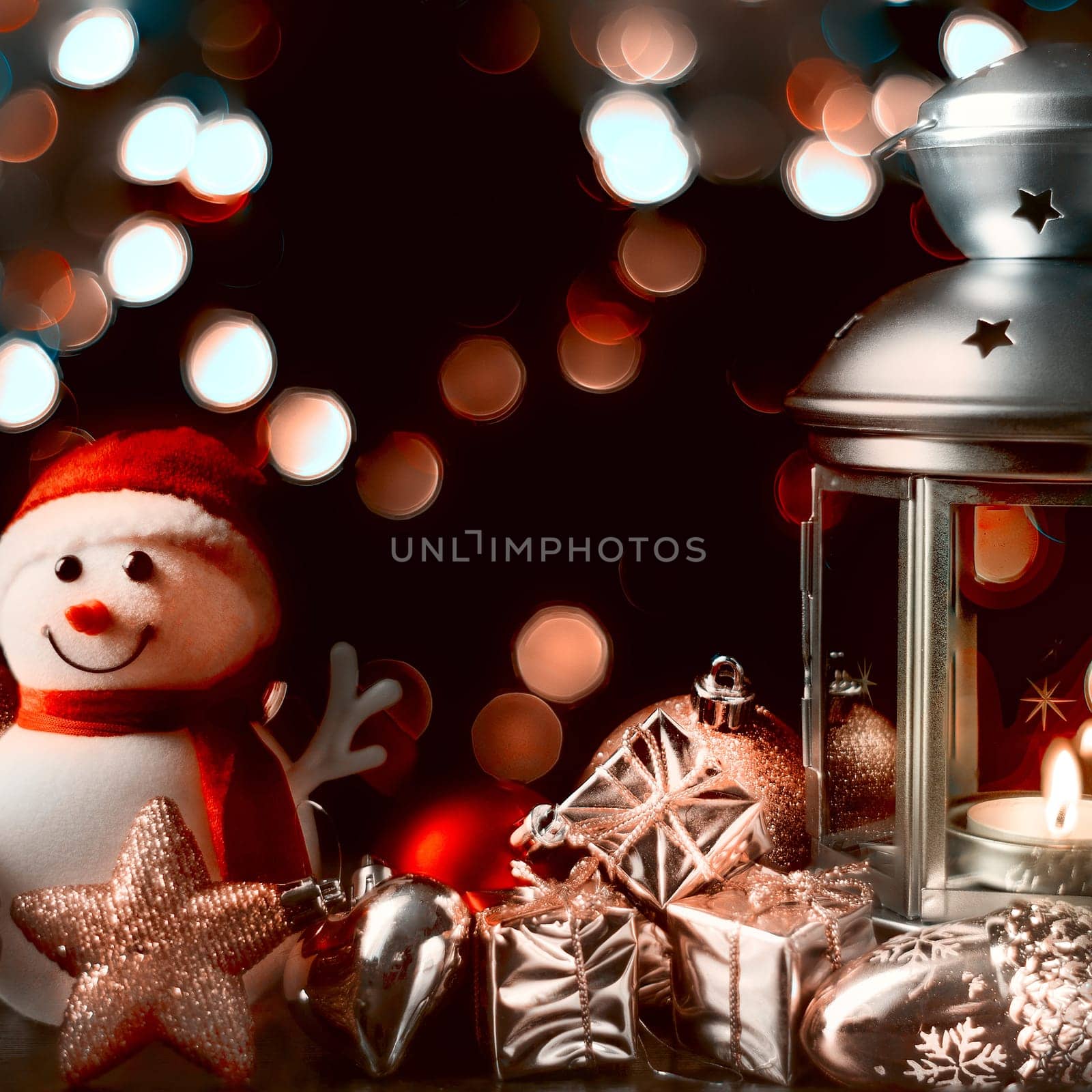 Christmas composition: A snowman, a lantern with candles, bright shiny boxes with gifts, blurred bokeh lights in the background.