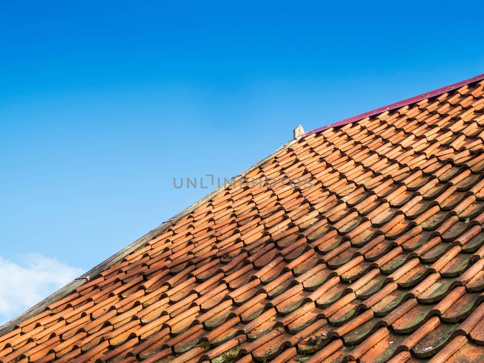 Oblique lateral partial view of a pitched roof covered with shingles in bottom view in front of a cloudless sky in sunshine.