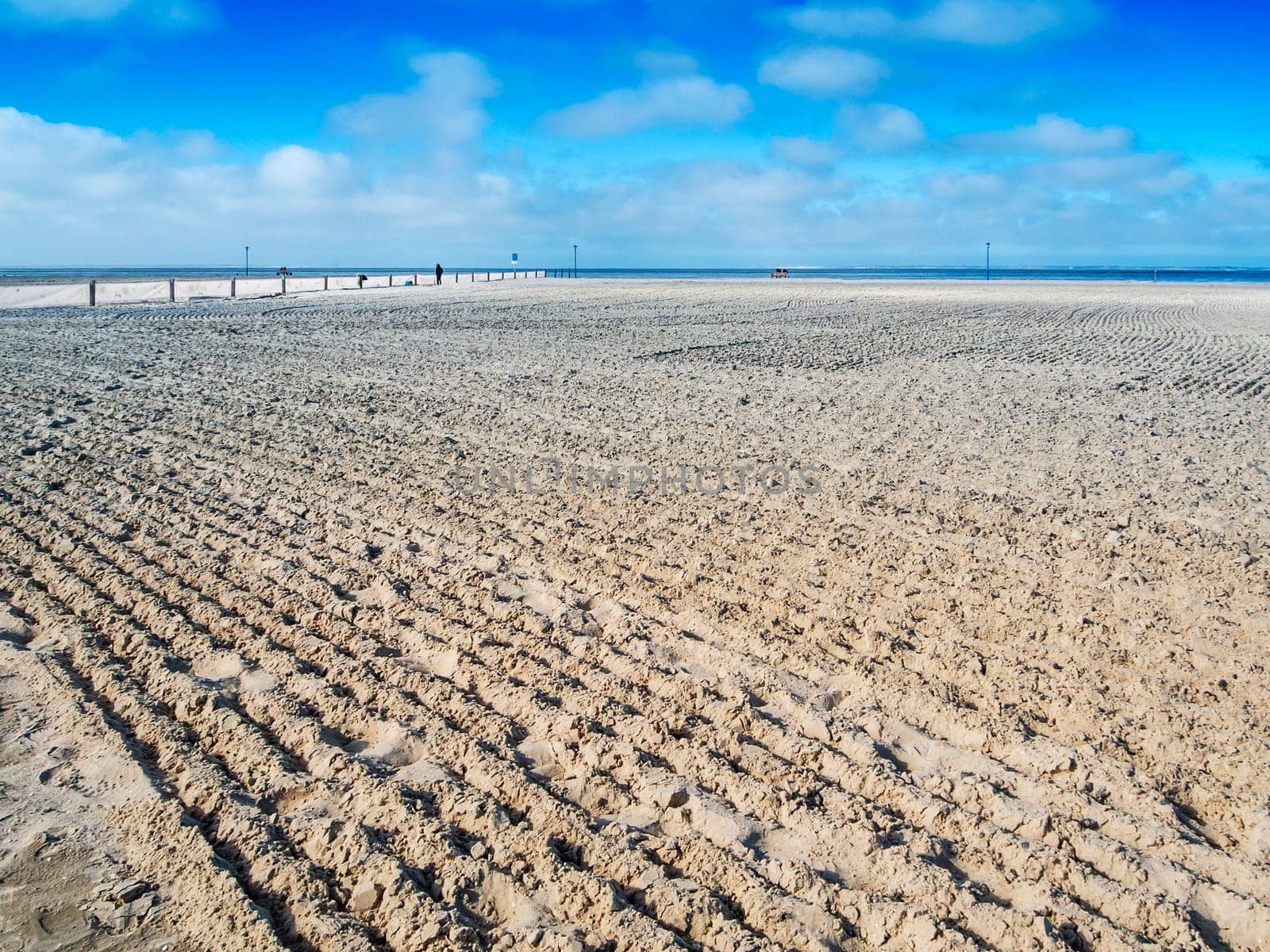 Landscape view of the German North Sea beach near Neuharlingersiel with a freshly smoothed empty sunbathing beach in front of a blue sky with some clouds in spring and a view to the horizon.