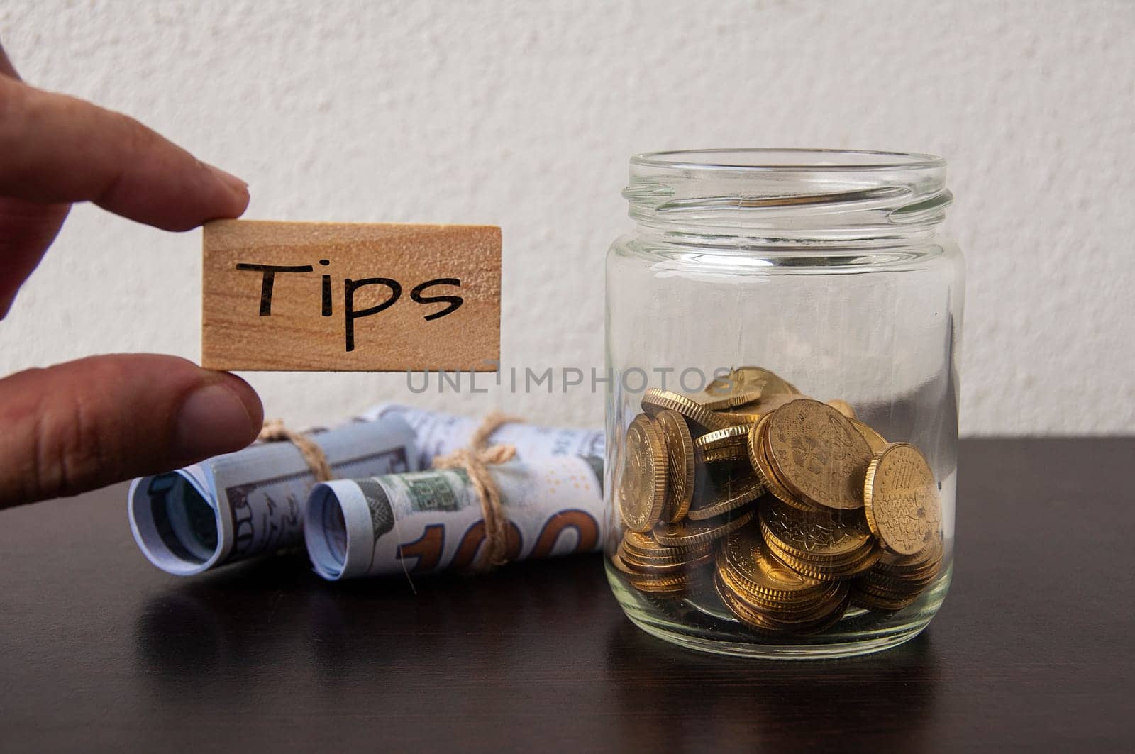 Hand holding wooden block with tips text. With gold coins and bank notes background.