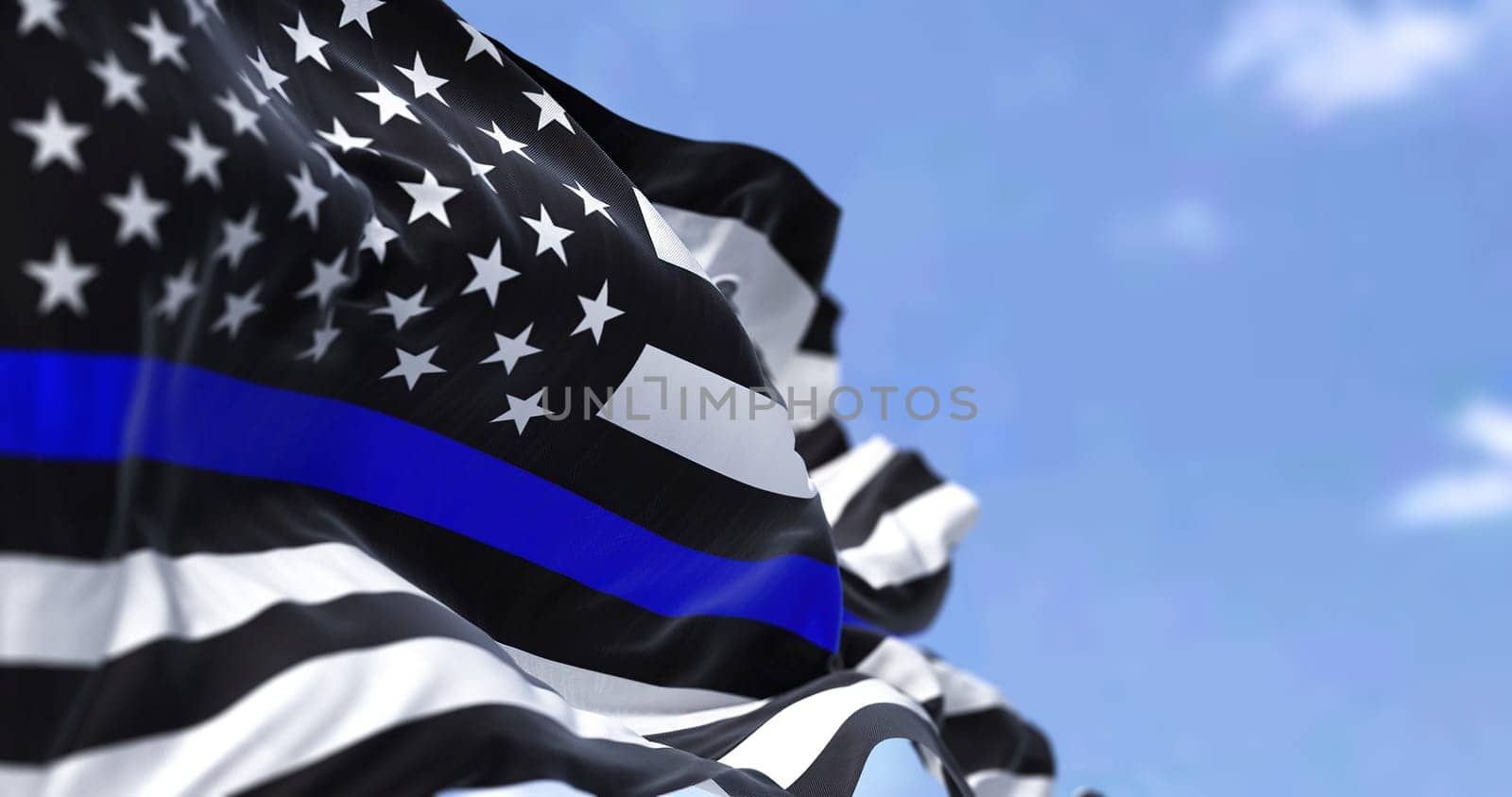 The flag of the United States of America in the Thin Blue Line variant waving in the wind. The "Thin Blue Line"" flag is all black, bearing a single horizontal blue stripe across its center"