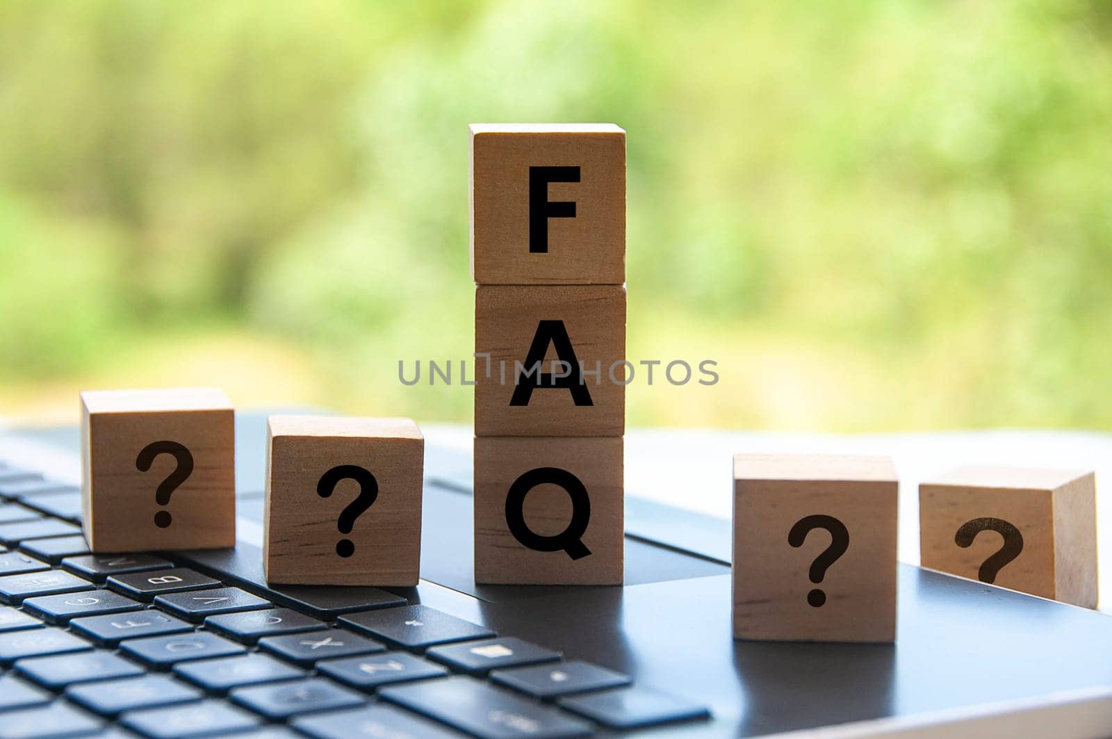FAQ word on wooden block on top of laptop with blurred nature background.