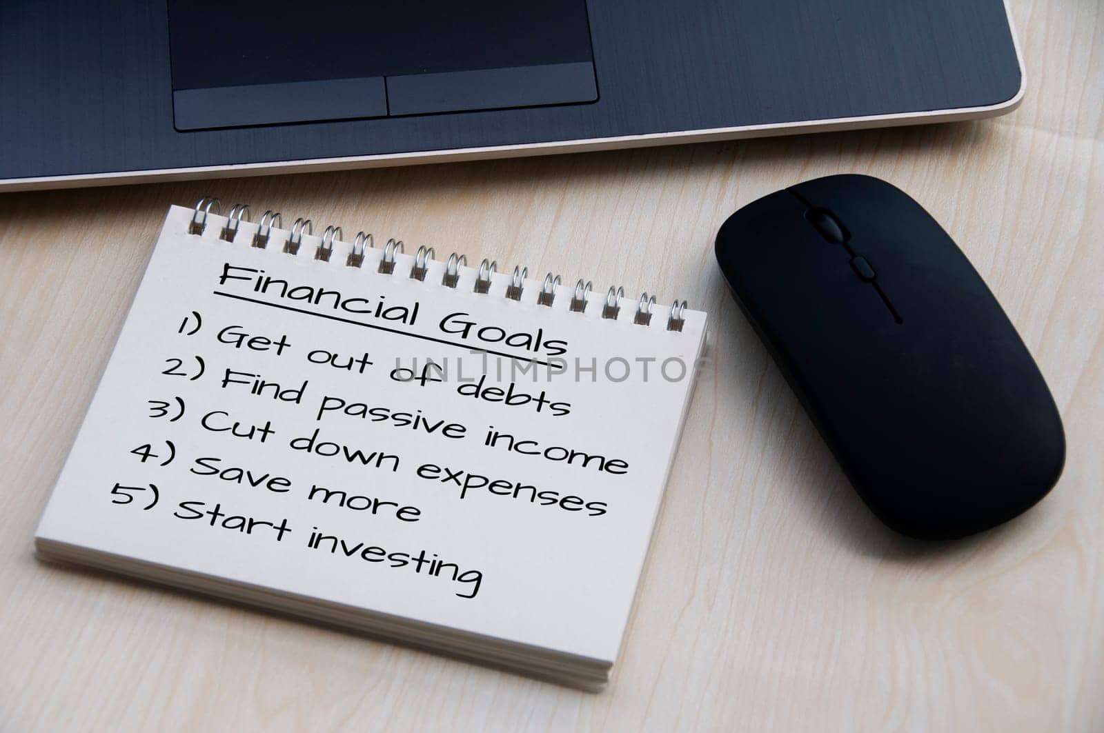 Financial goals on notepad on blank notepad with laptop and mouse on a wooden table, retro style.