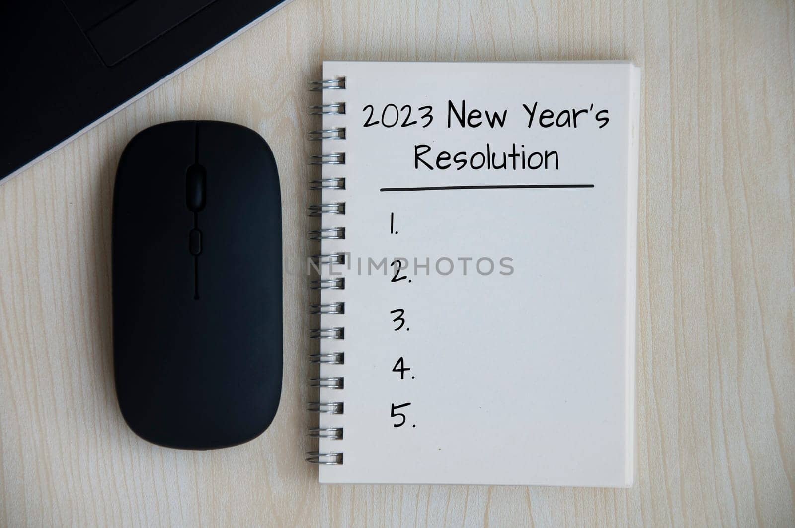 2023 New Year's Resolutions text on note pad with mouse and laptop on wooden desk.t