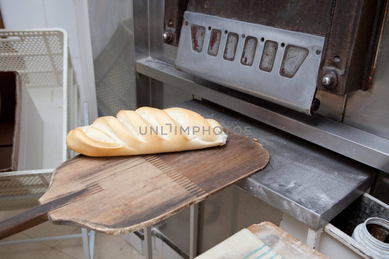 Baker taking fresh baked bread from oven. Manufacturing process of spanish bread