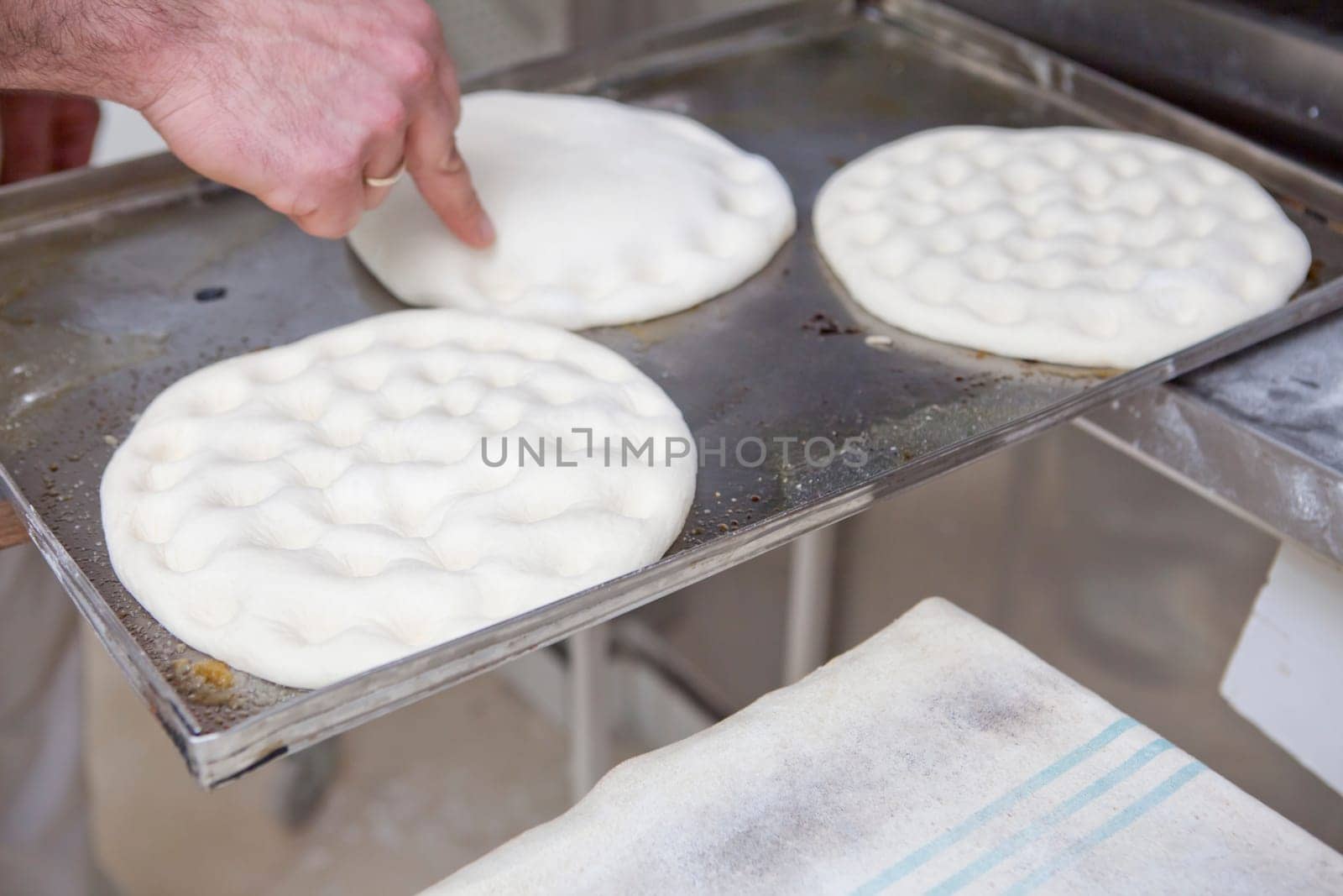 Elaboration of traditional spanish olive oil pancakes. Baker making holes on raw bread using his finger to shape the dough prior baking