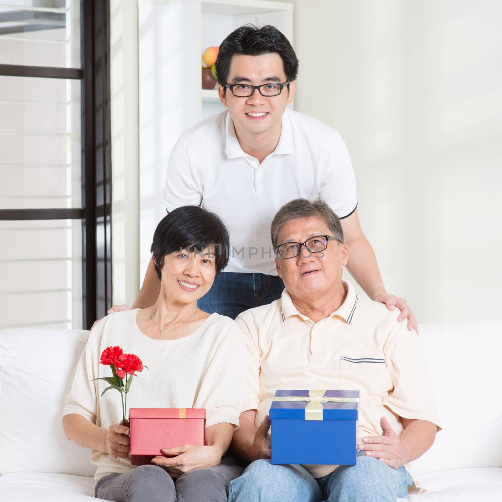 Asian senior parents receiving gift from their child. Family at home.