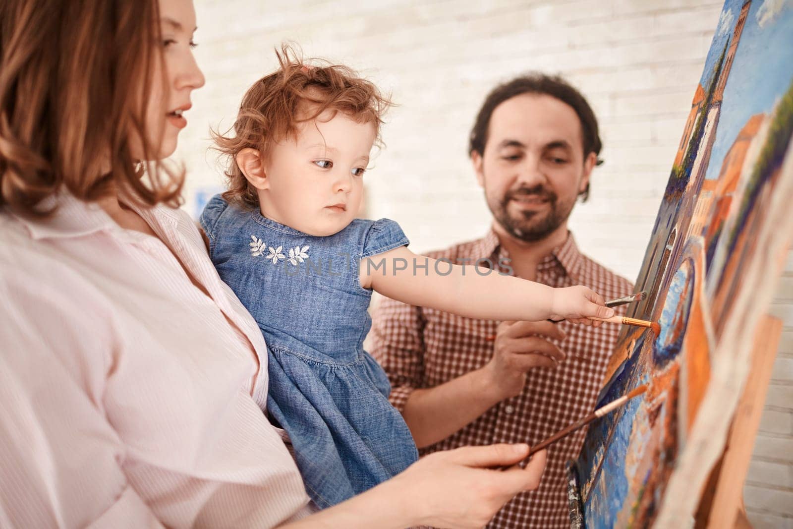 Young parents teaching their daughter how to paint
