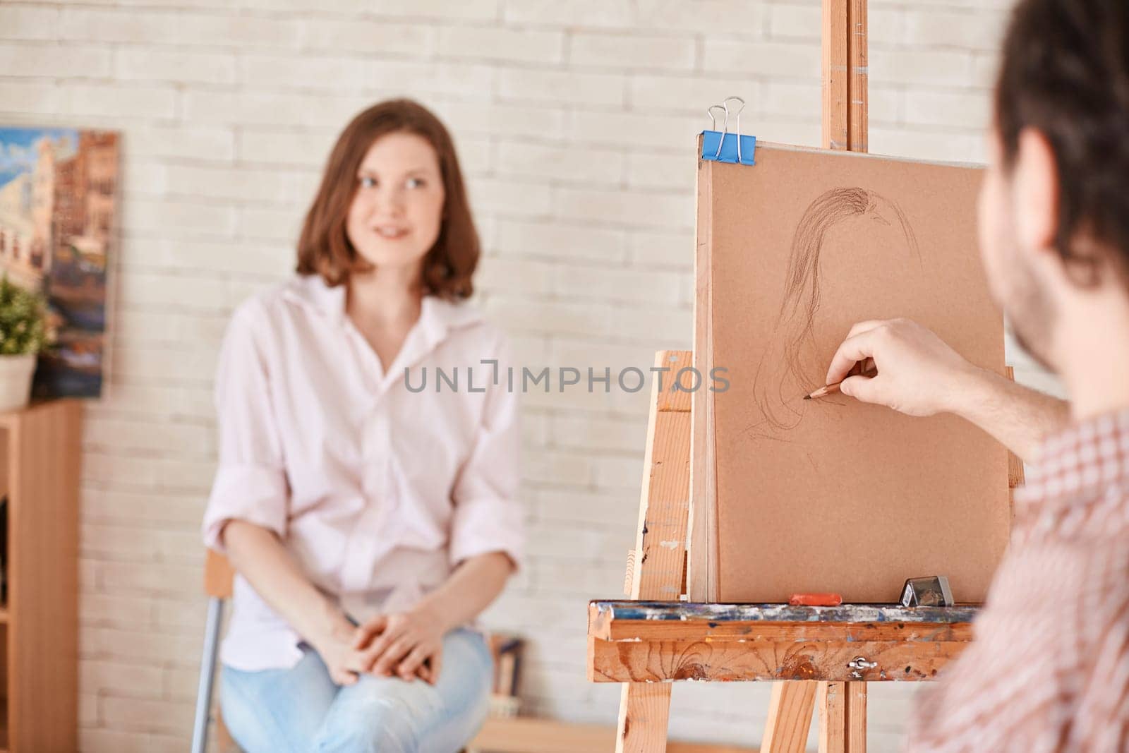 Male artist drawing young woman in studio