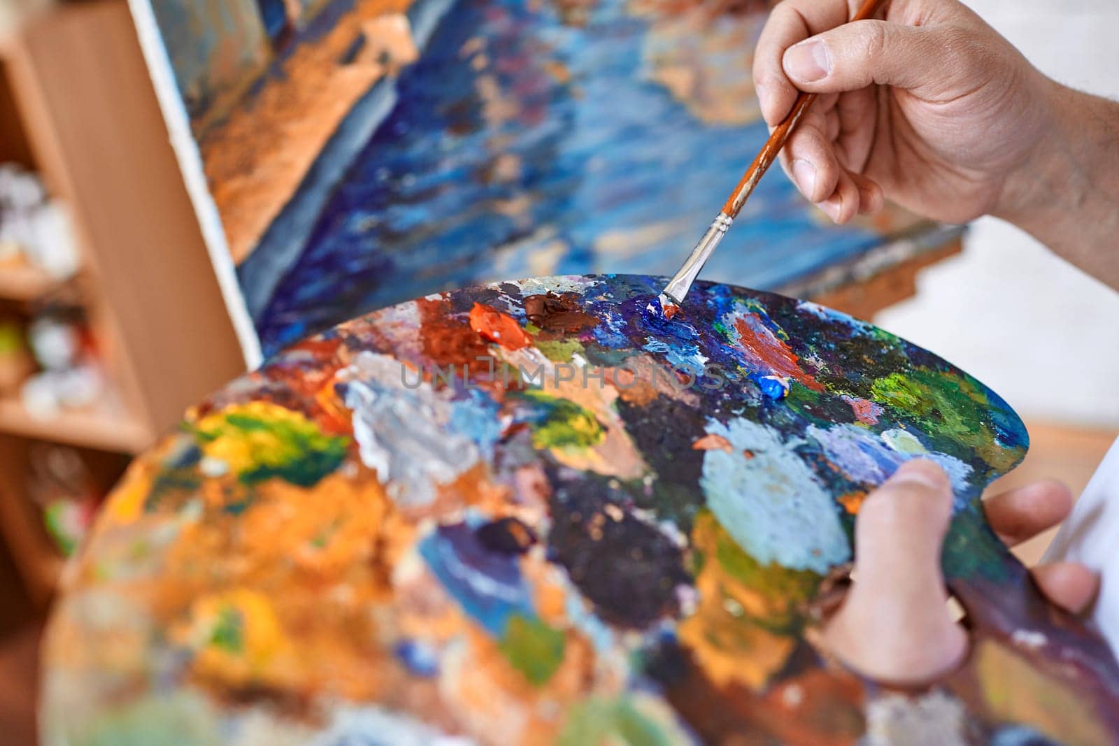 Hand of artist with paintbrush mixing oilpaints