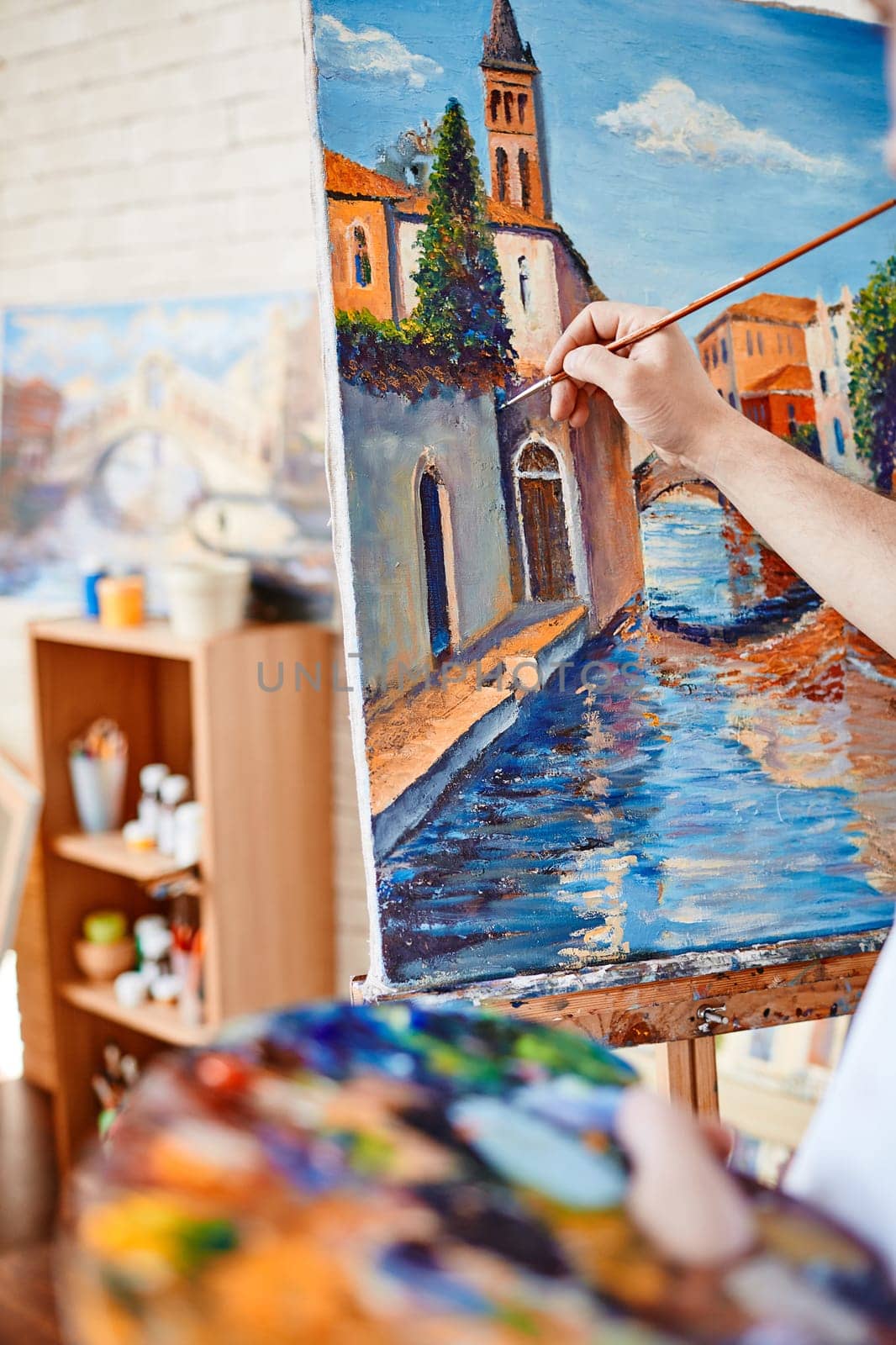 Hand of artist painting street of Venice on canvas