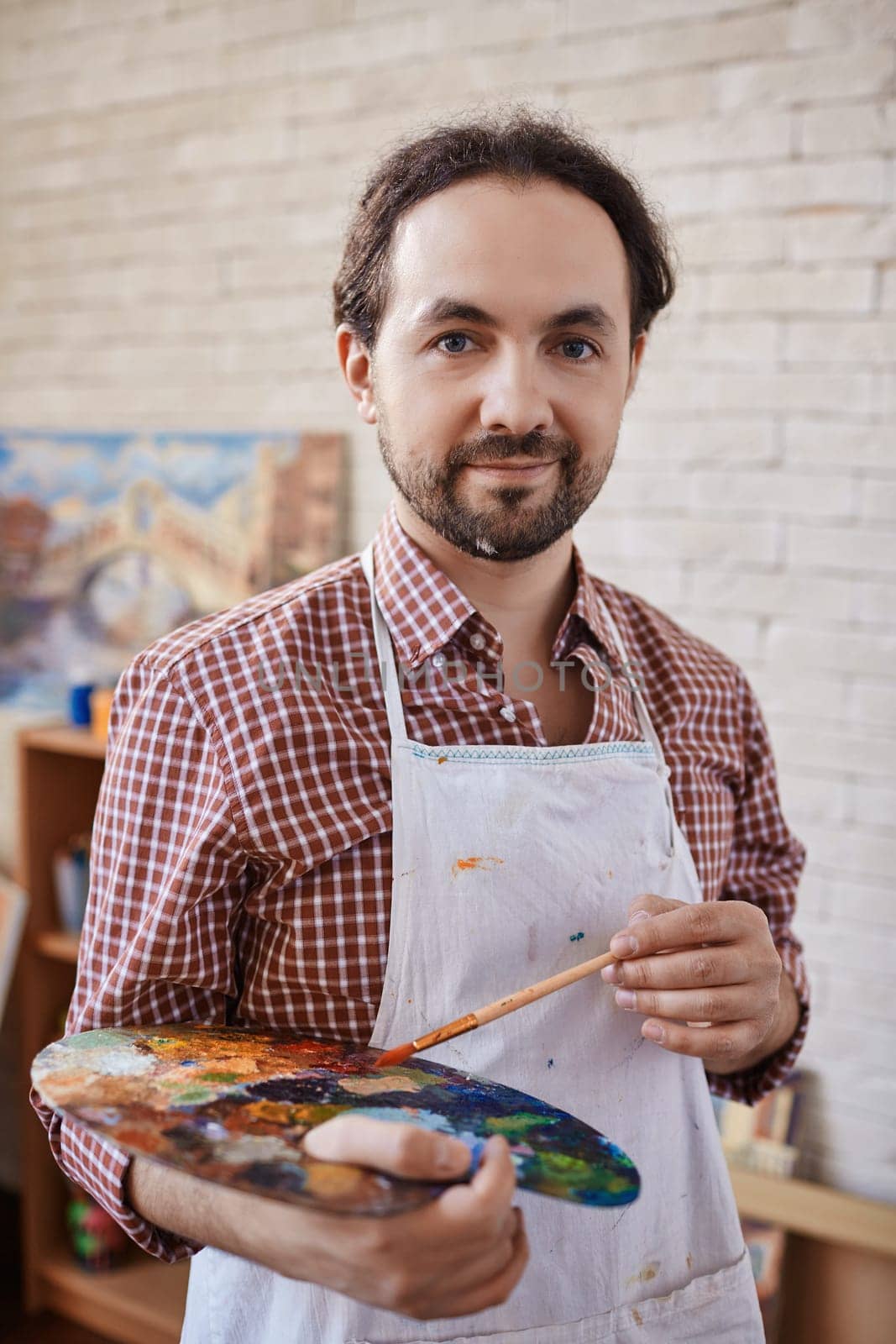 Modern artist with paintbrush and palette looking at camera in studio