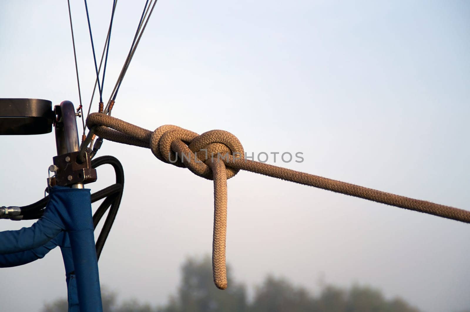 A strong rope is tied to the cables of a hot air balloon to hold it to the ground on a foggy morning. Balloon is not shown.