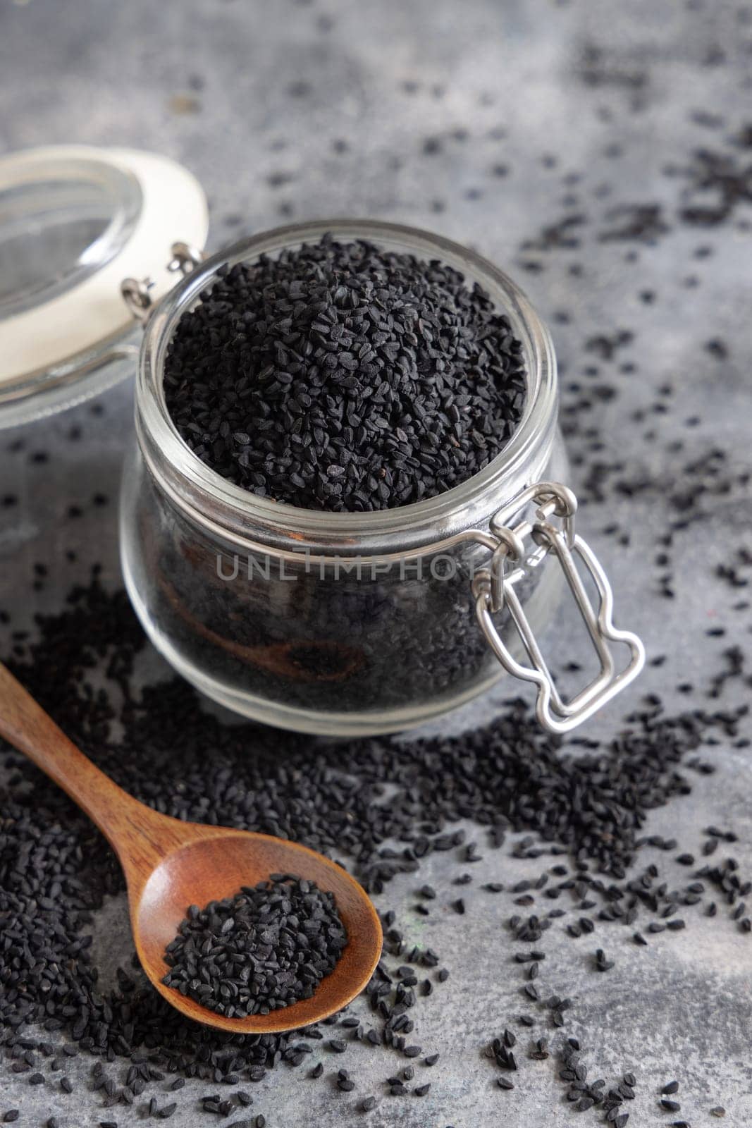 Indian spice Black cumin (nigella sativa or kalonji) seeds glass jar with a wooden spoon, close up. Traditional asian medicine, healthy and vegetarian food concept