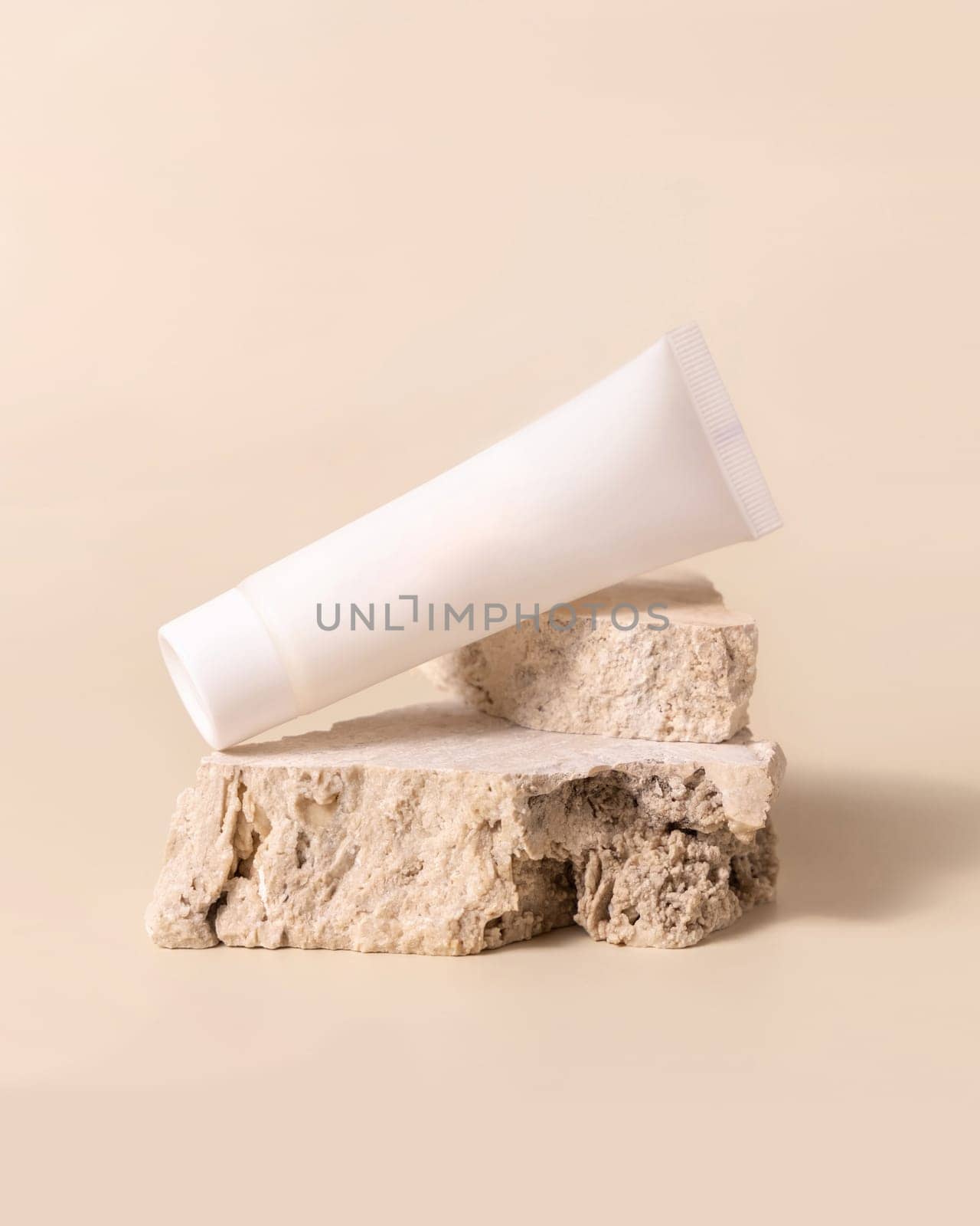 White plastic cream tube on travertine stone on light yellow, close up, mockup. Skincare beauty product. Natural cosmetics. Minimal composition..