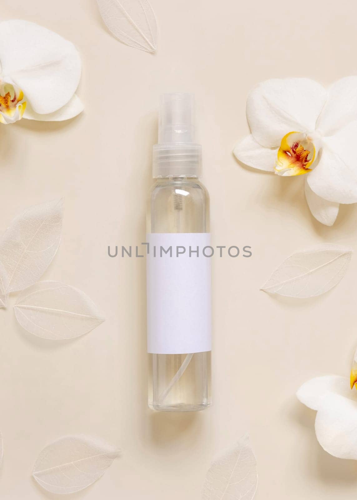 One pump dispenser bottle near white orchid flowers on light yellow top view, mockup. Skincare beauty product package. Exotic natural cosmetics, pastel minimal composition..