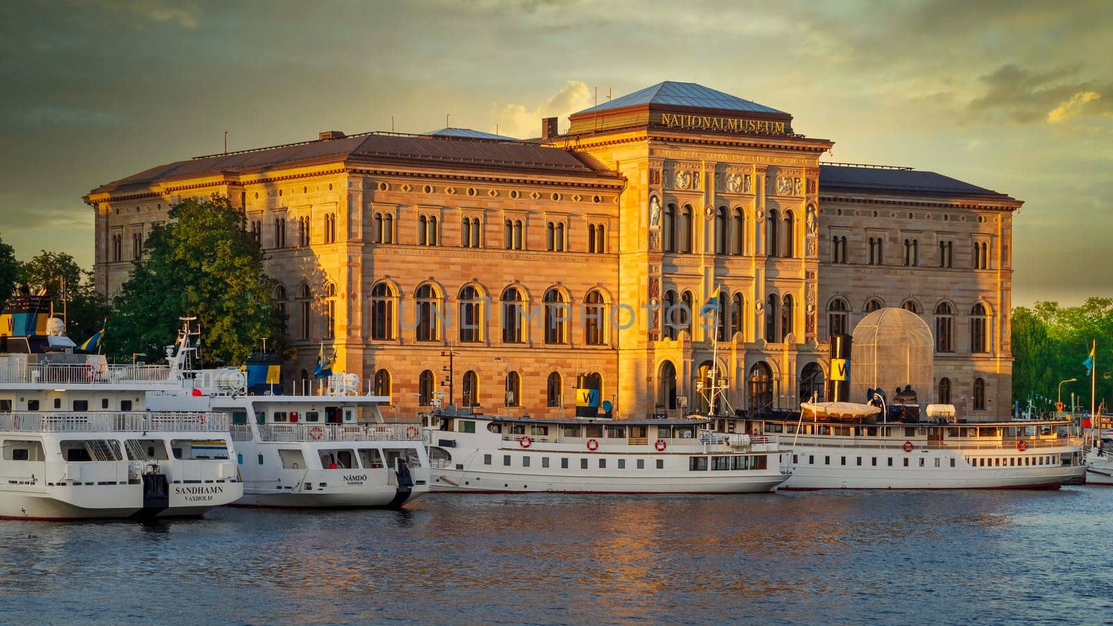 Nationalmuseum, or National Museum of Fine Arts, located on the peninsula Blasieholmen in central Stockholm, Sweden - View from Stockholms stromo with ferries parked in front at sunset in a summer day