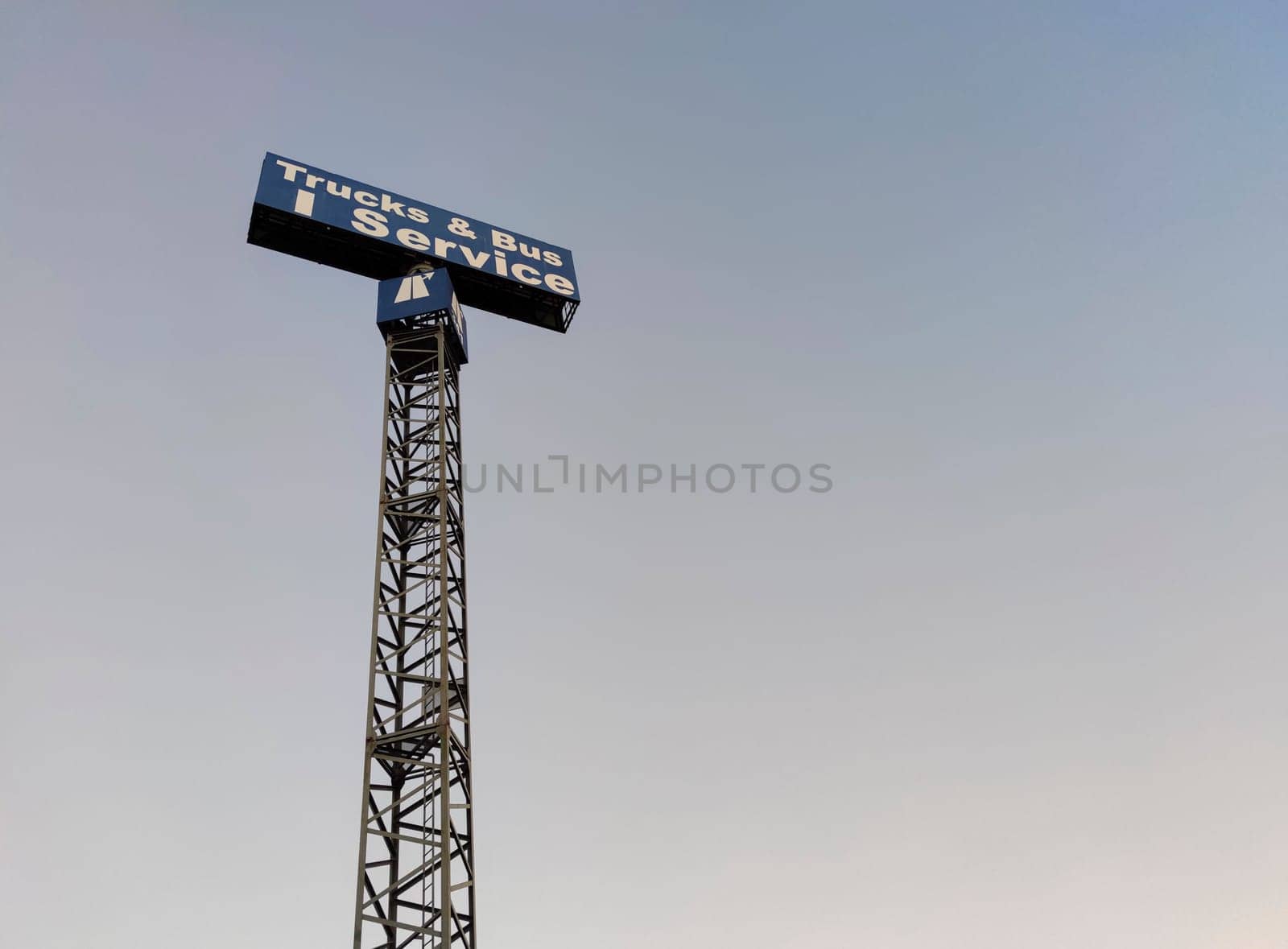 Trucks and bus service sign pole over blue sky.